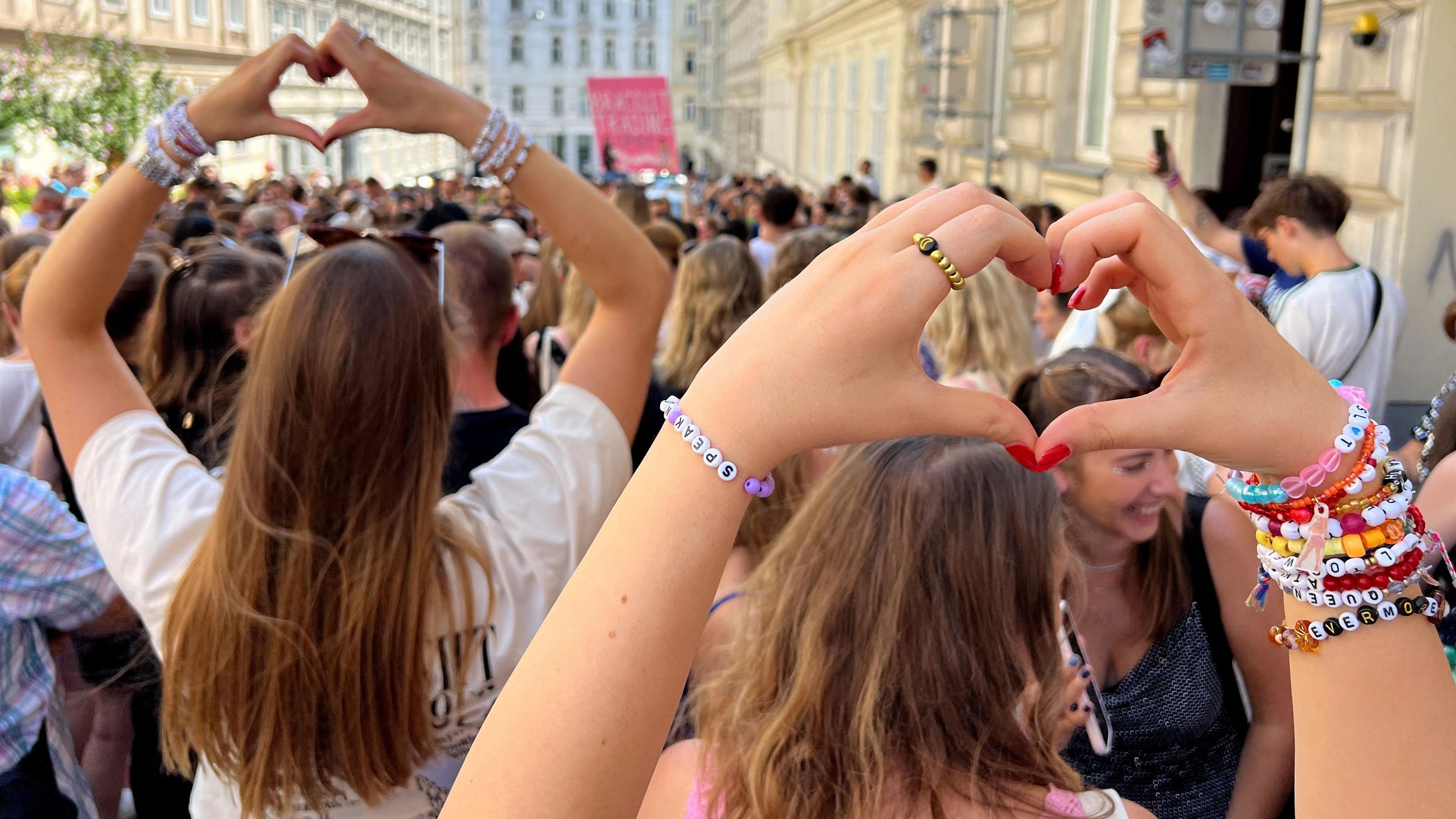 A crowd of fans on a Vienna street with some wearing bracelets and making heart shapes with their hands