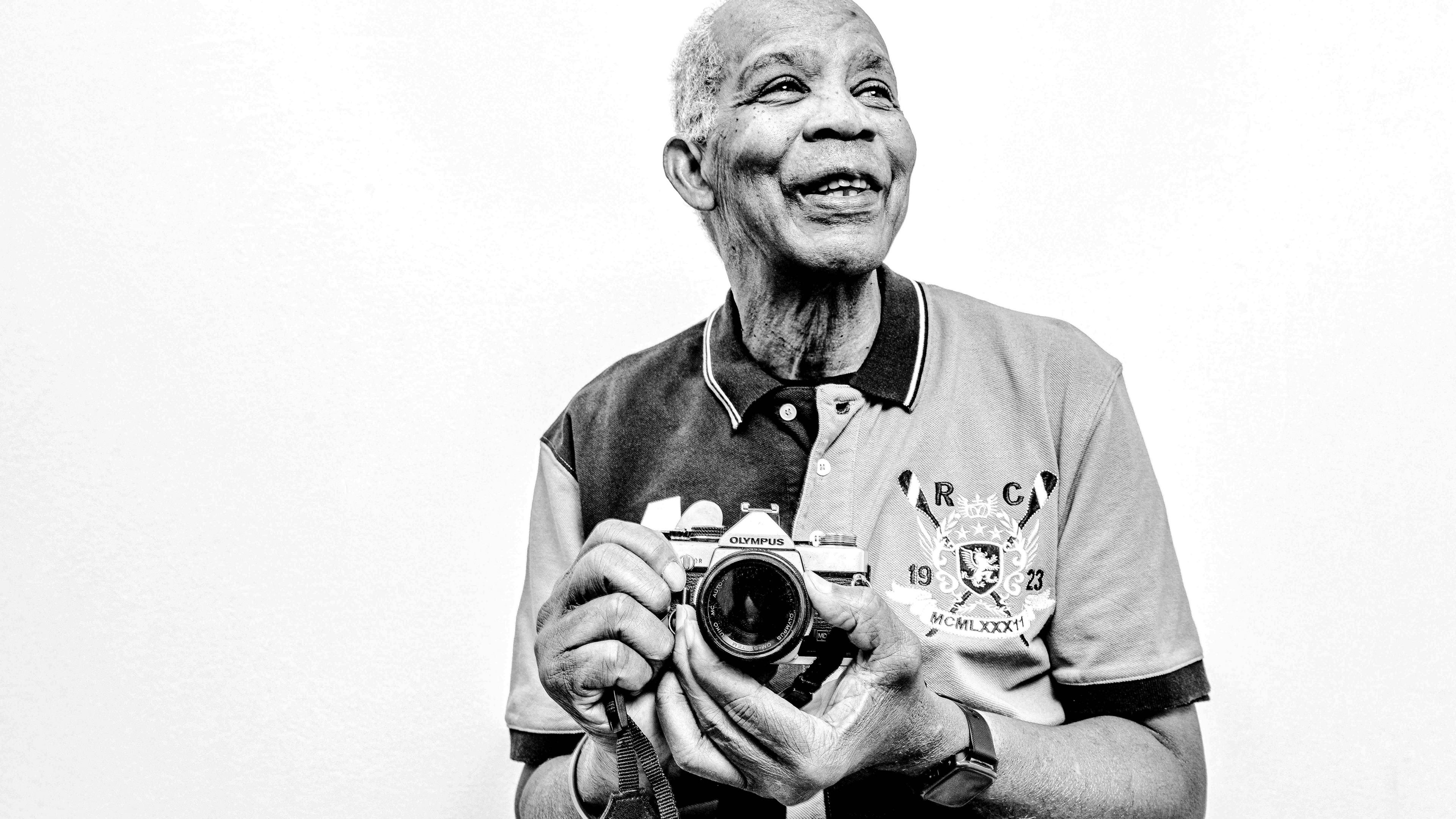 An older man holds a camera and smiles.