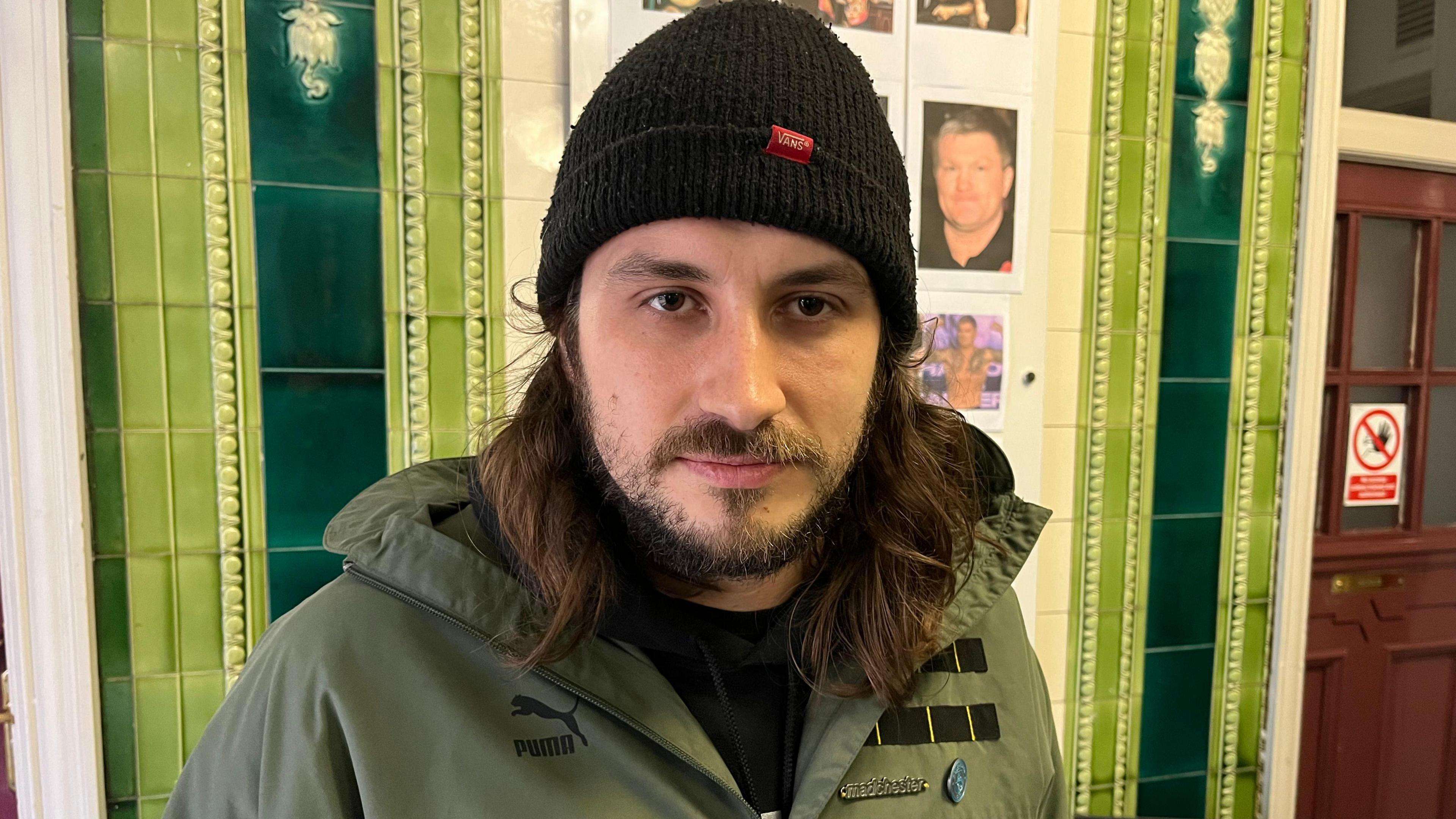 Deggie, 32, who is wearing a woolly black hat over shoulder length brown hair and a dark green Puma brand coat, looks into the camera. 