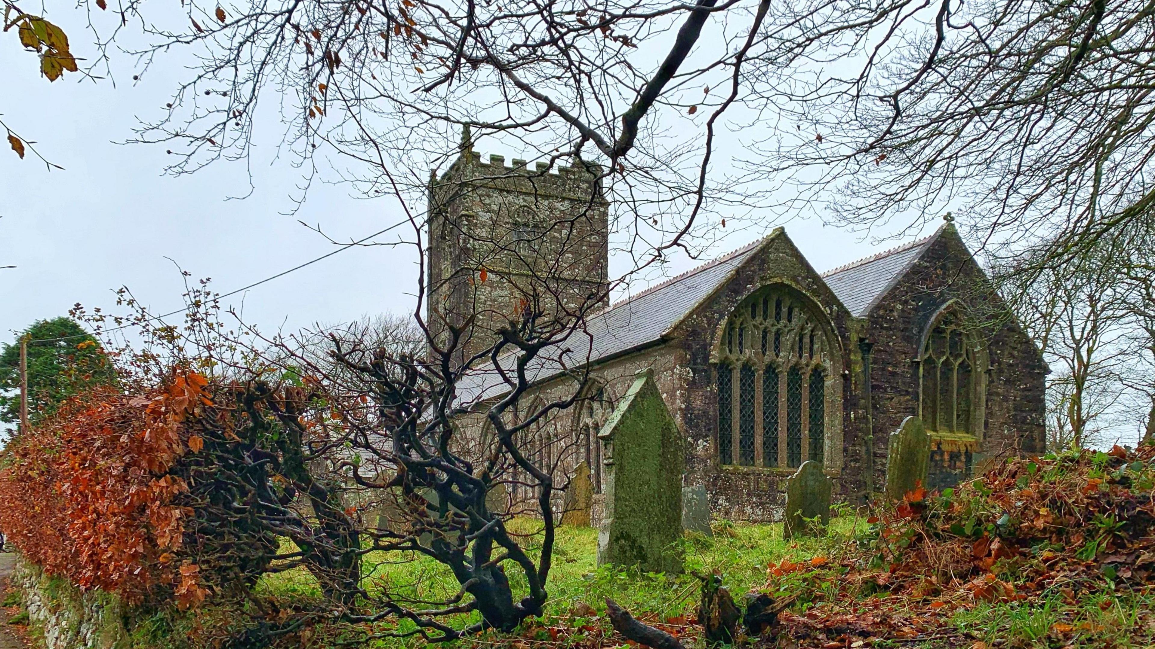 Looking through the hedges at St Breward Church with old gravestones in the foreground 