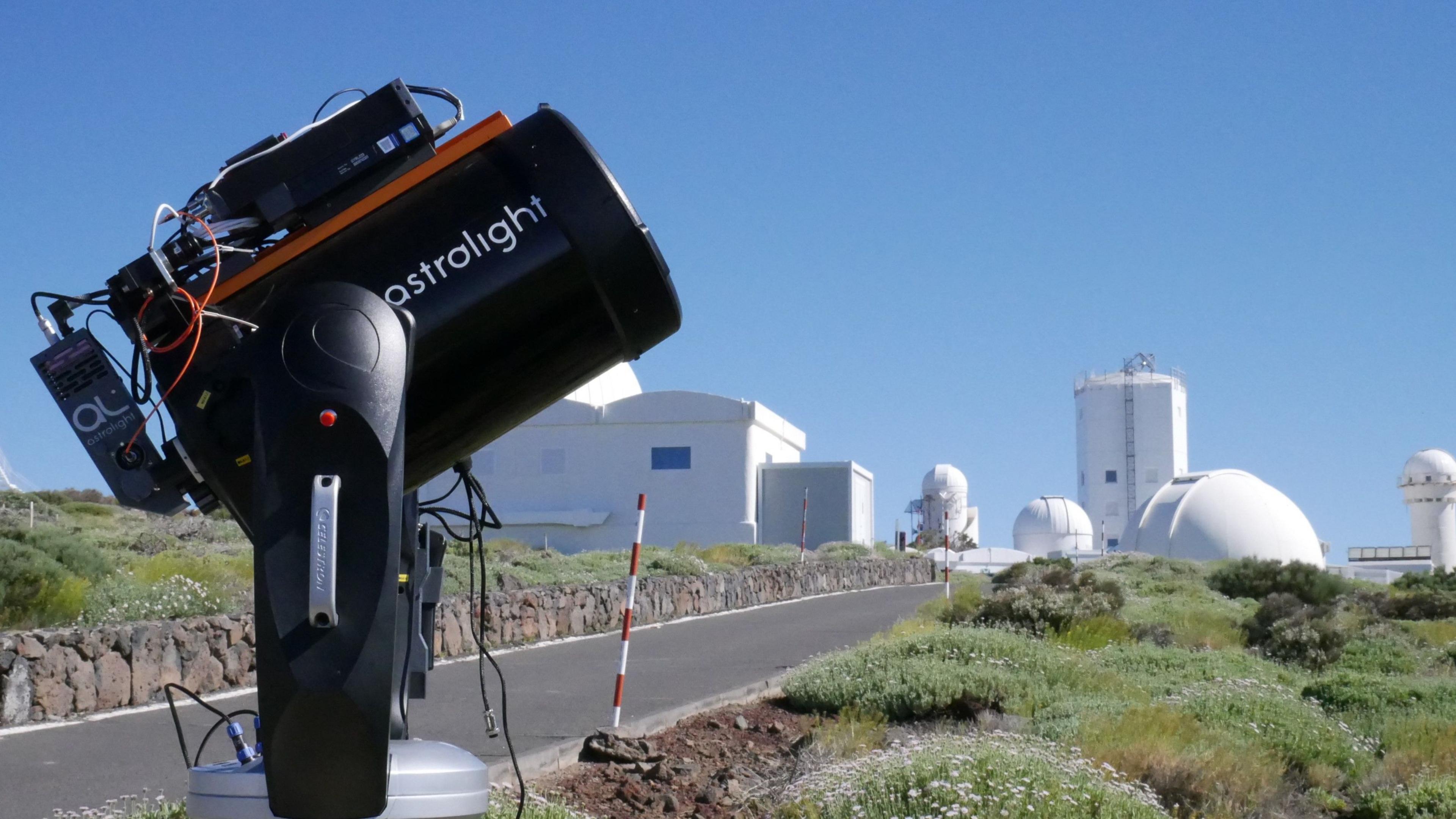 An Astrolight laser points towards the sky with telescopes in the background