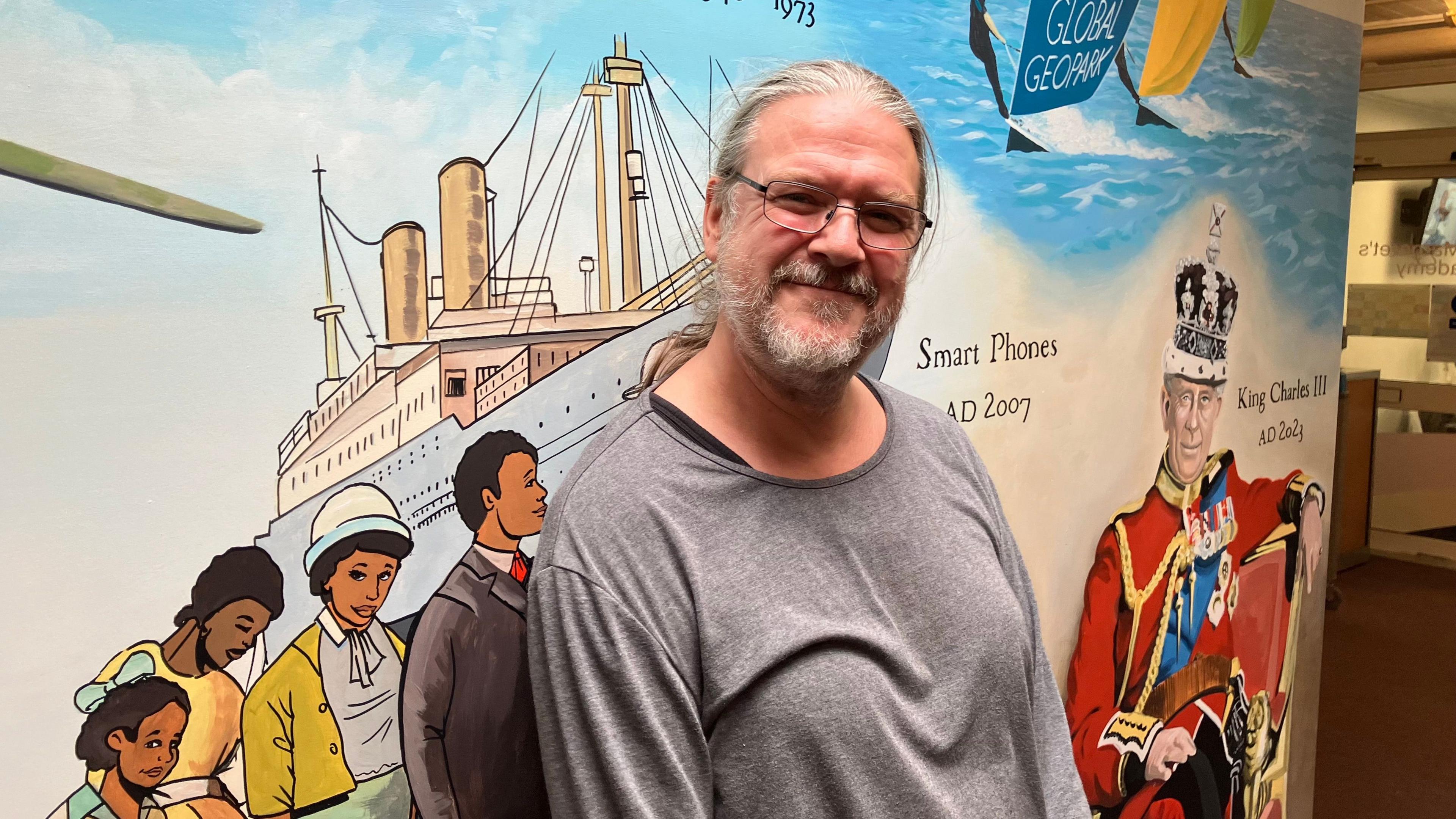 Artist Neil Wilkinson-Cave standing in front of his mural at St Margaret's Academy