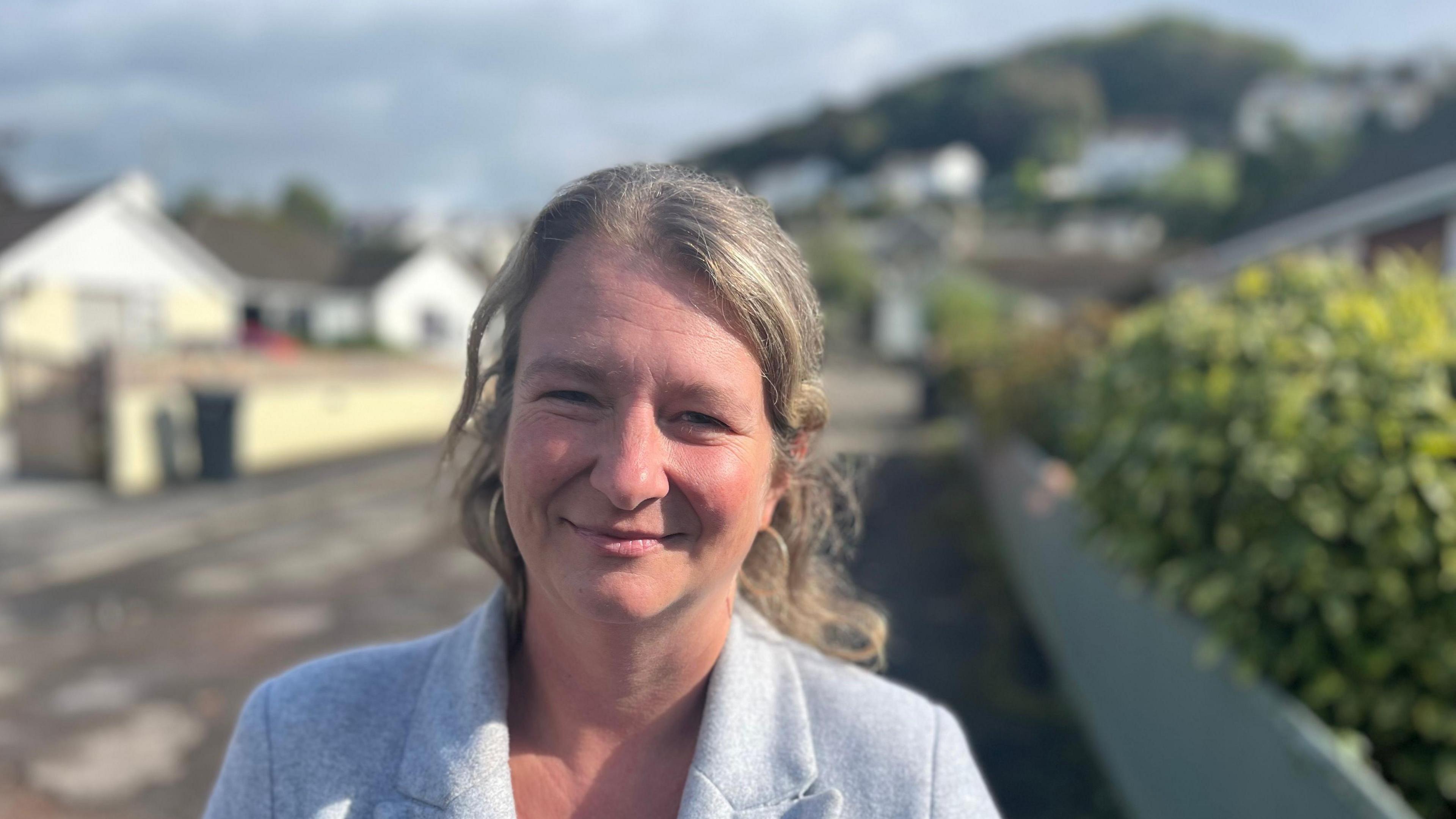 Emma Hookway, a founder member of the campaign group, North Devon and Torridge Housing Crisis, wearing a grey jacket and standing on the pavement with bungalows in a slightly blurred background