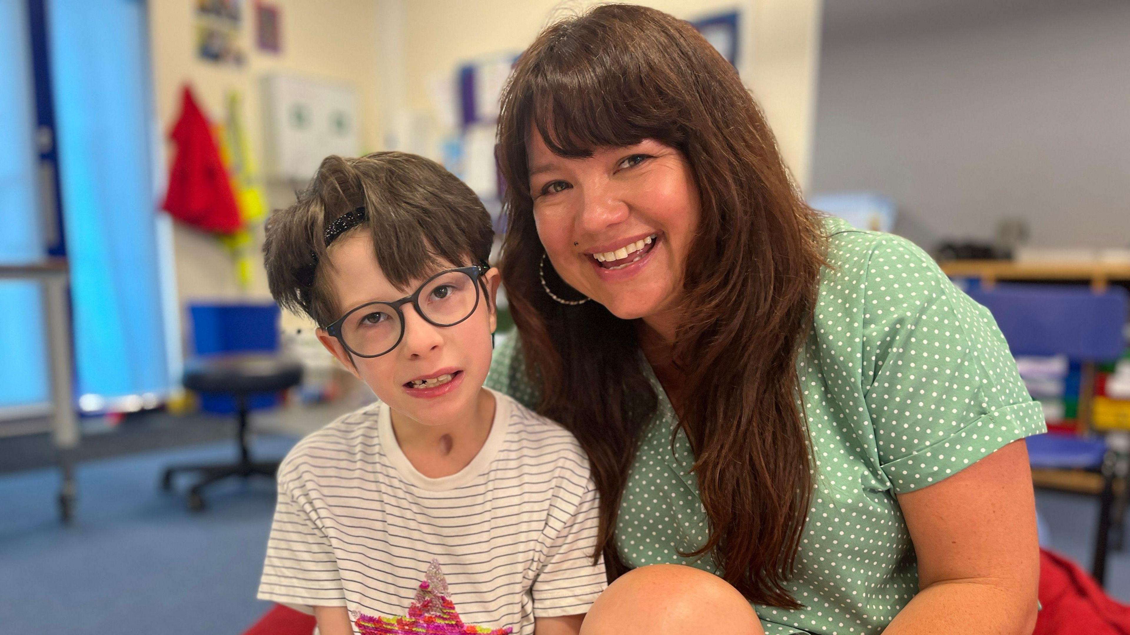 A boy wearing glasses and woman smiling wearing green polka dot top