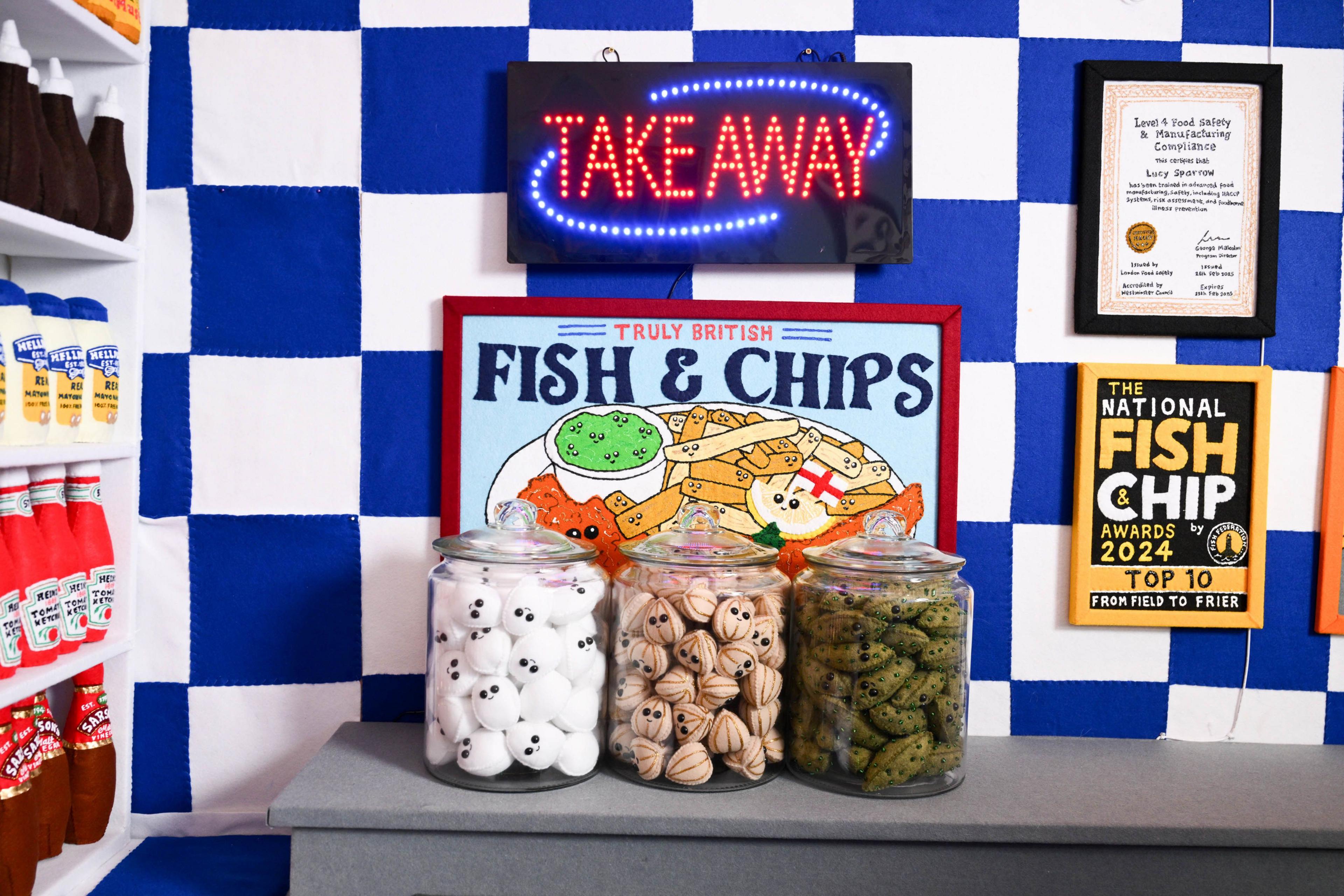 Three jars sit on a grey felt counter, in front of a sign that reads 'Fish and Chips'