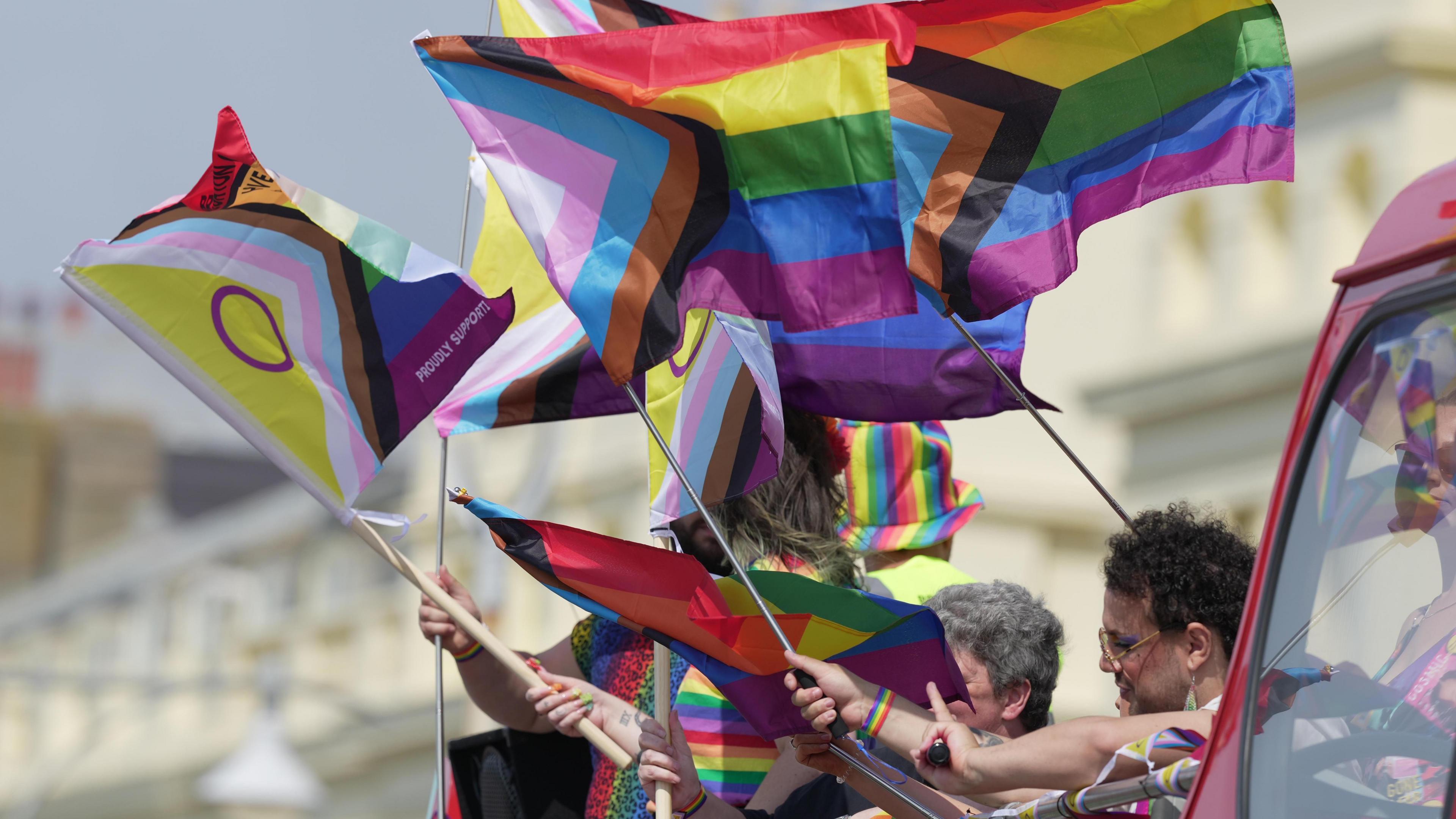 People onboard an open top bus waving rainbow and trans pride flags