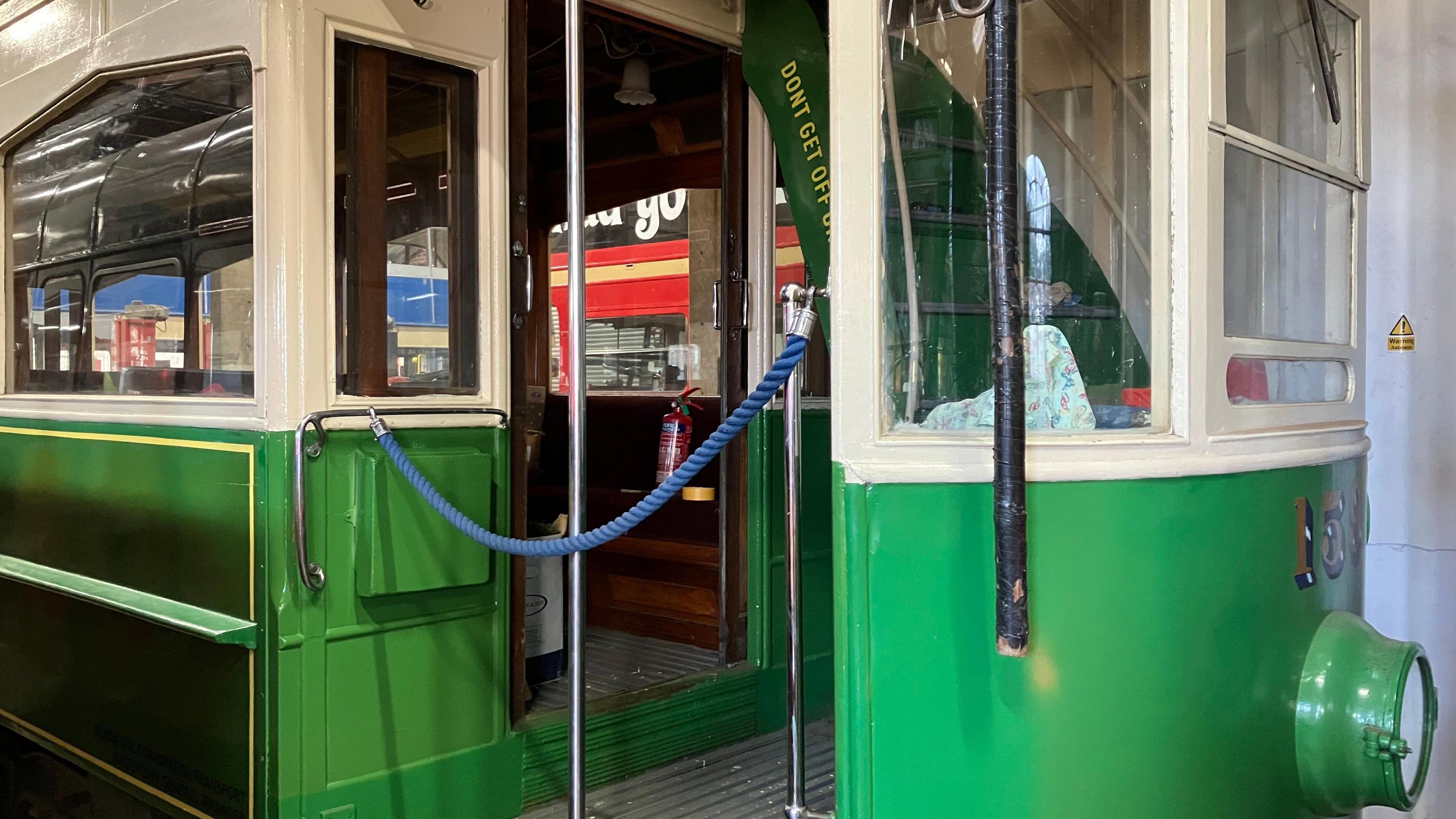 The entrance to a green and white tram with a silver metal rod down the centre of the gangway and a blue cord hanging up over the entrance