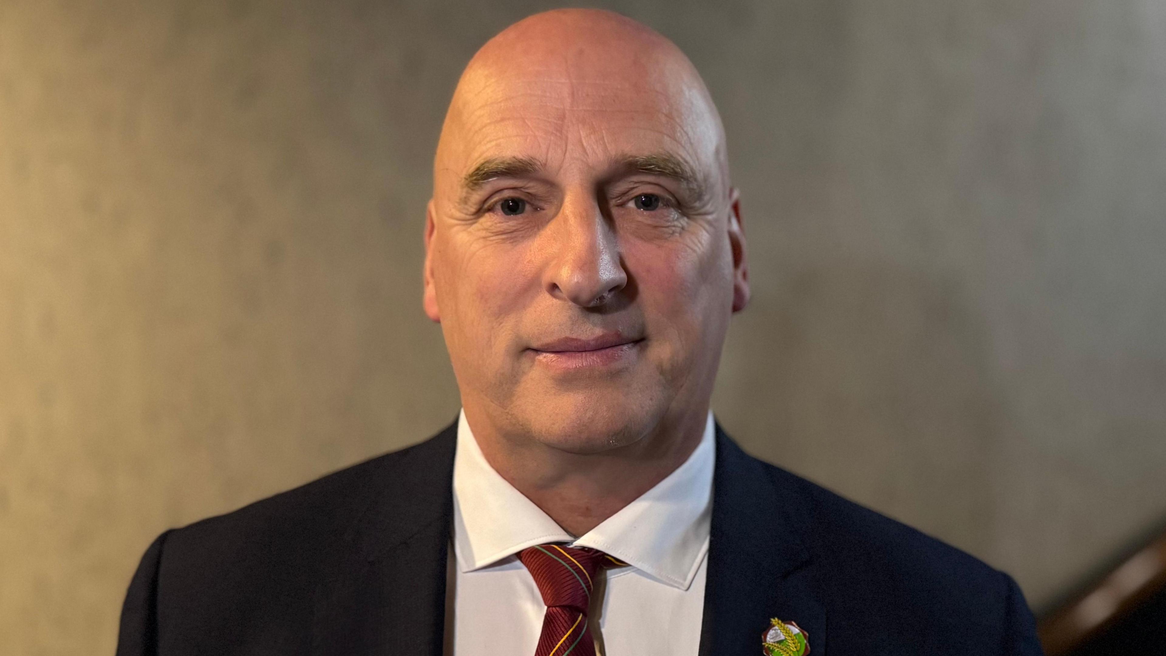 A man wearing a dark blazer and white shirt with red tie