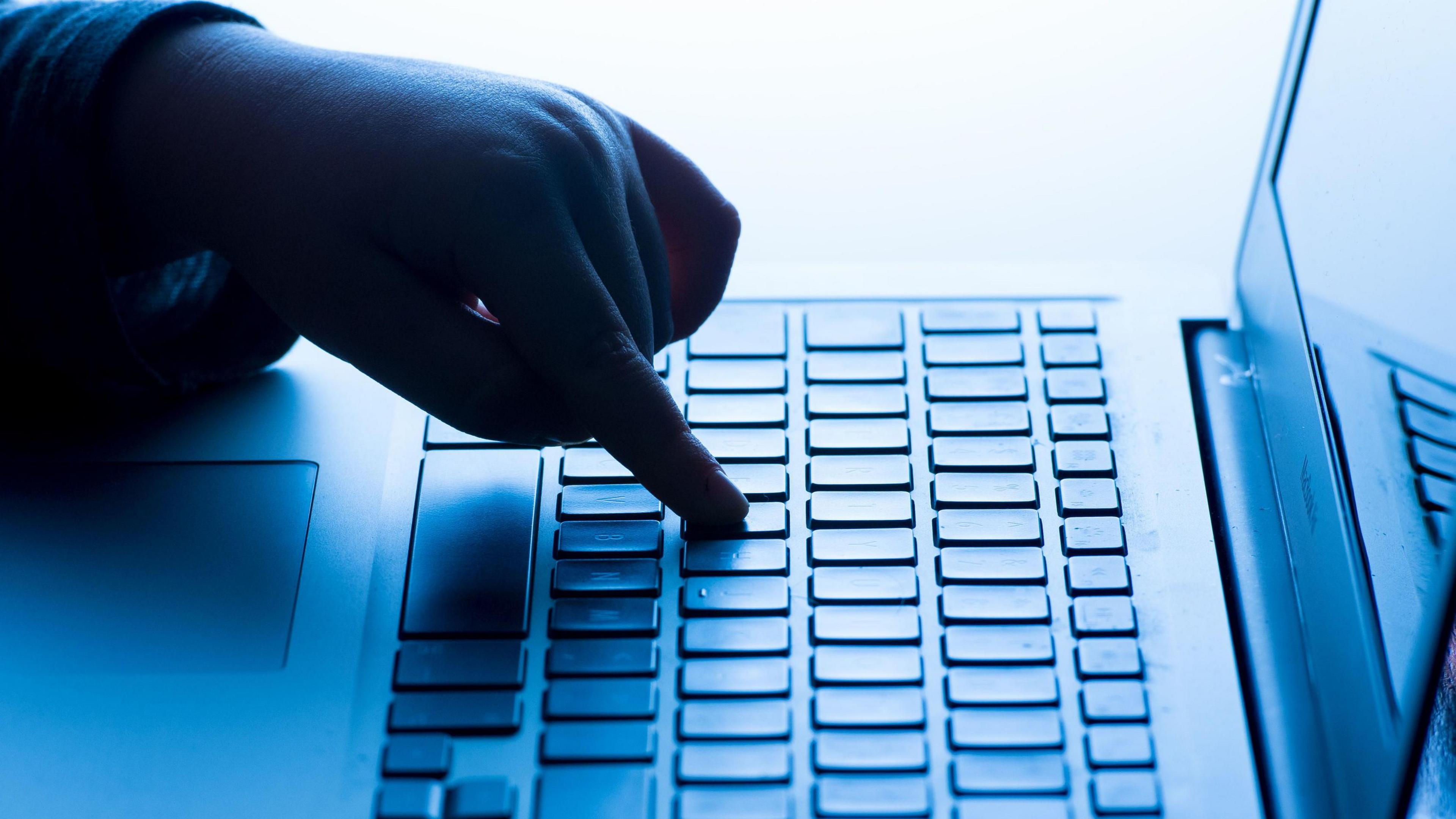 A child's hand is on a laptop keyboard with a screen to the right.