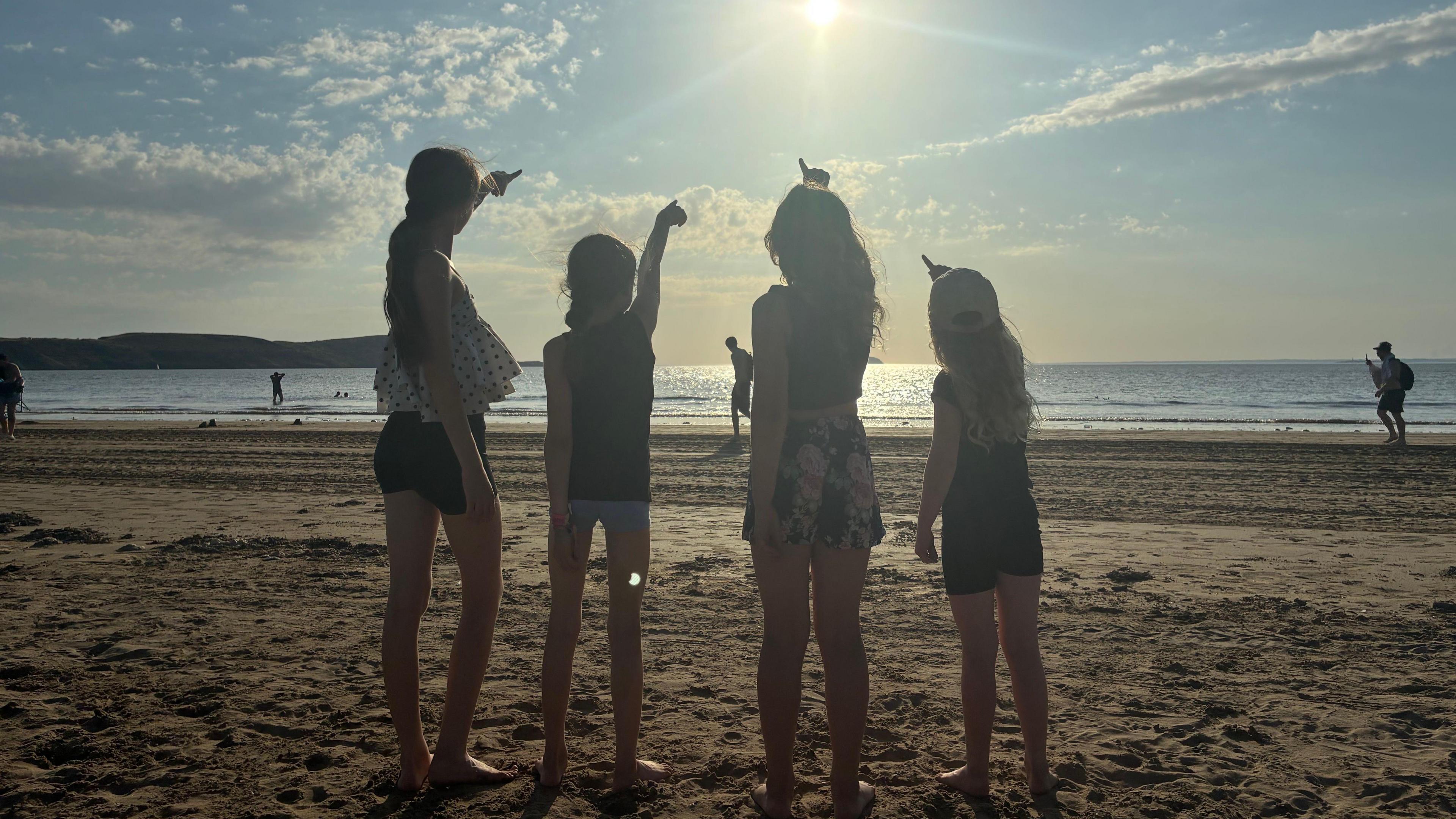 Four young girls are pointing up at the sky while standing on a sandy beach