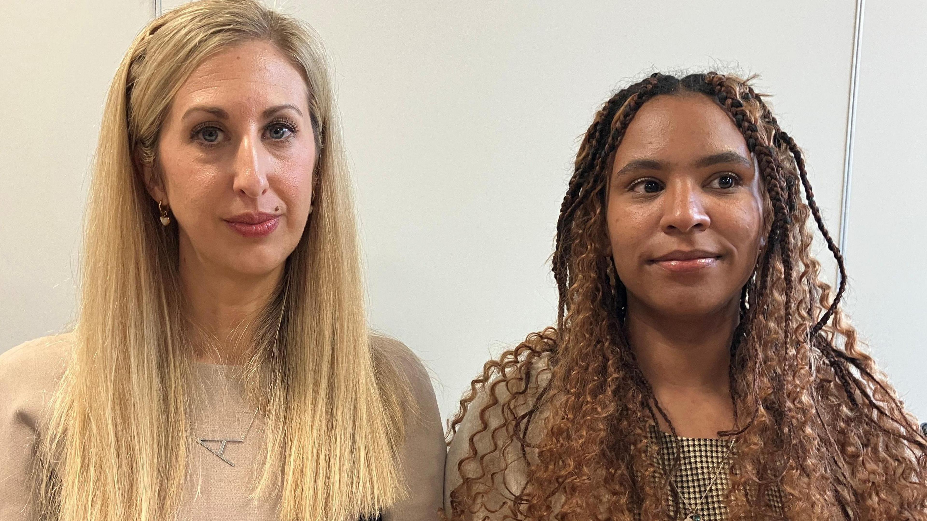 Two women sit side by side facing the camera. Fiona on the left is tall with long blonde hair and a light pink/beige T-shirt. Lauren on the right has curly brown braids and a white and brown gingham top.