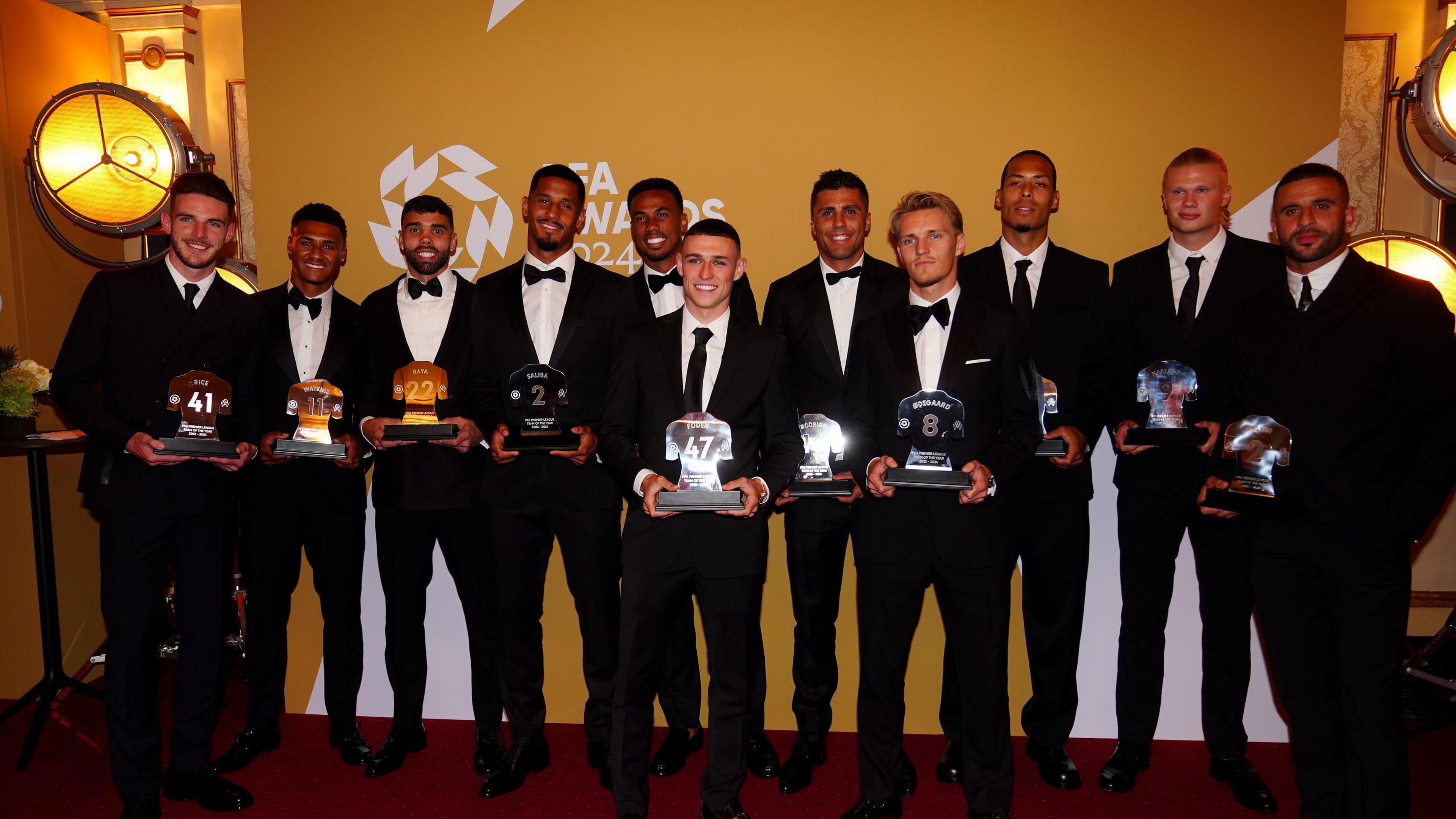 A squad of footballers in smart suits, including Phil Foden and Erling Haaland, hold their trophies at the PFA awards
