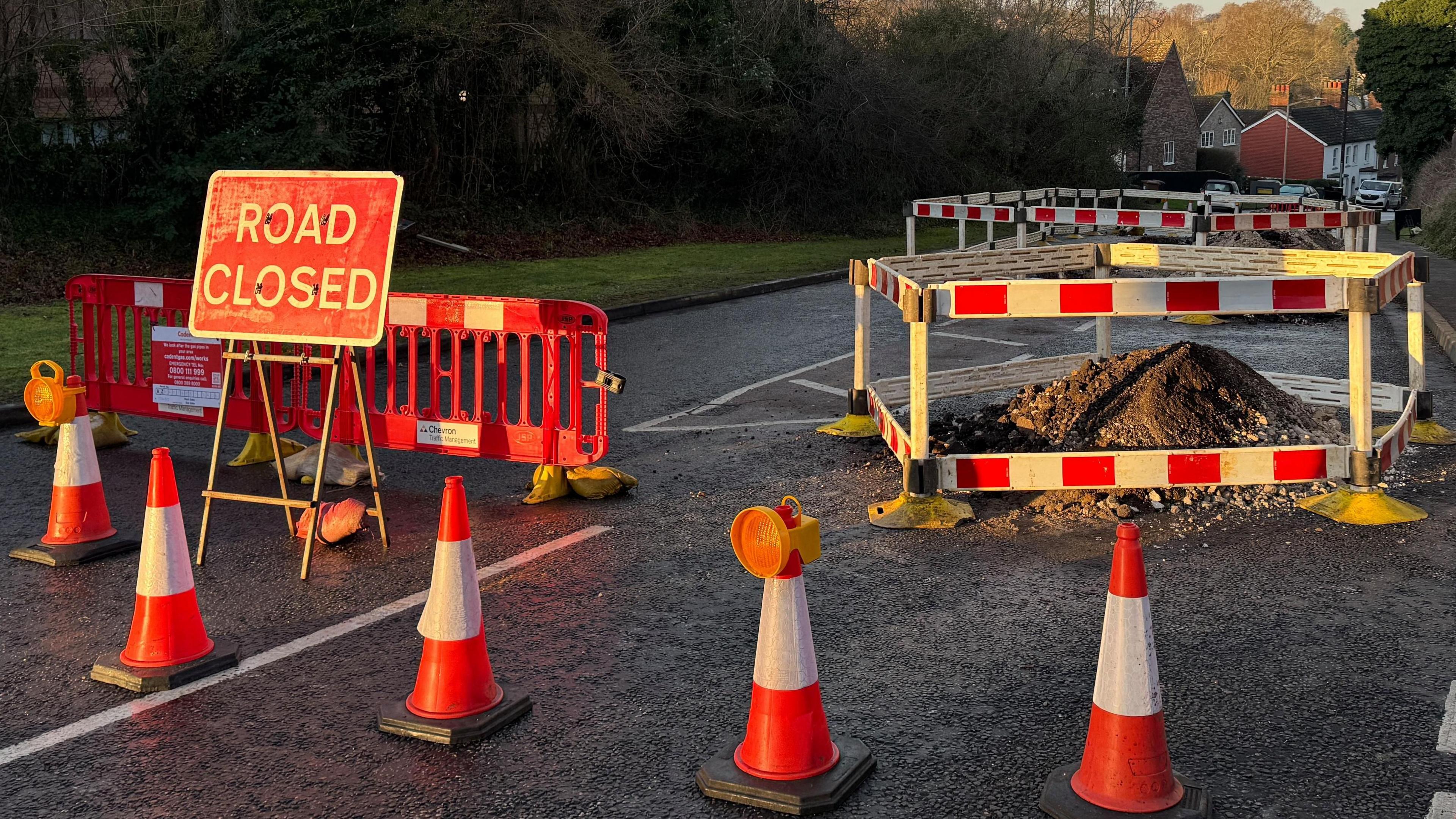 Road cones and a "road closed" sign on a road with areas cordoned off in the background which have been dug up by engineers.