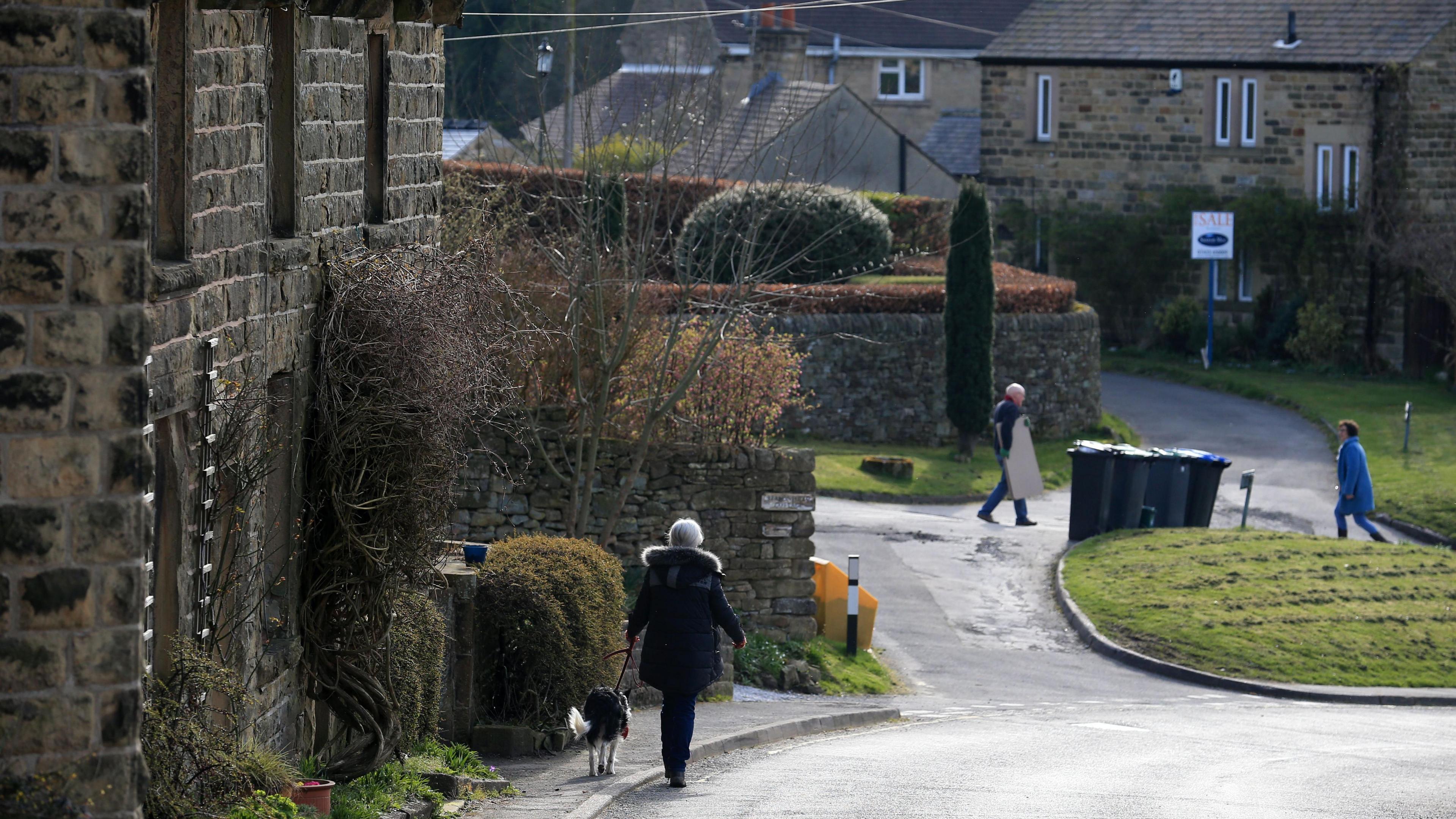 A photograph of the village of Eyam. There are a few cottages and people walking around the street 