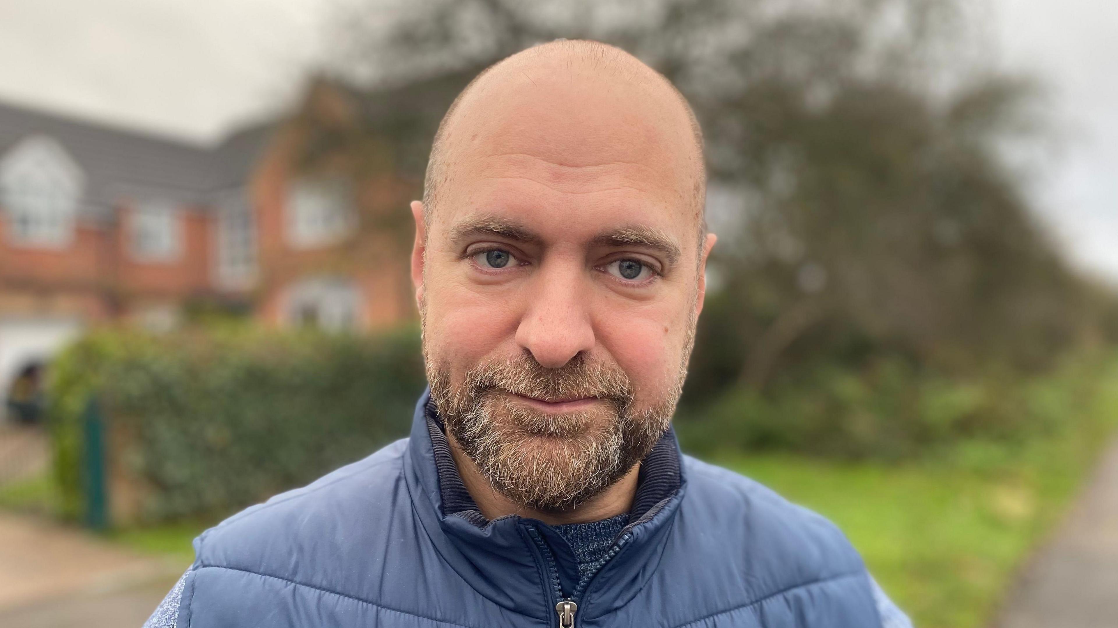 A profile image of Christopher Mallor, a bald man with a short greying beard wearing a blue, padded gilet.