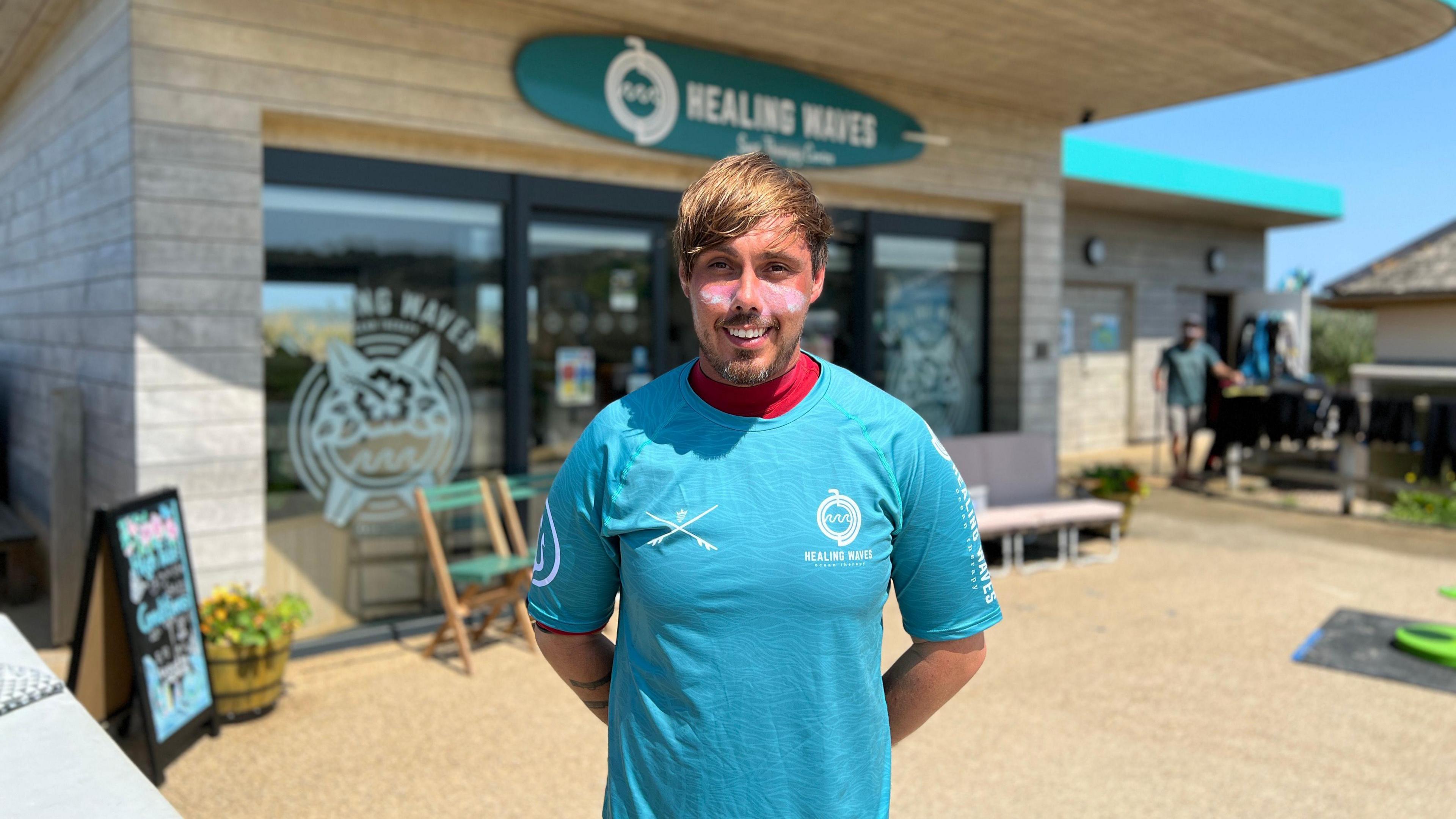 Max smiles at the camera as he stands in front of the Healing Waves office