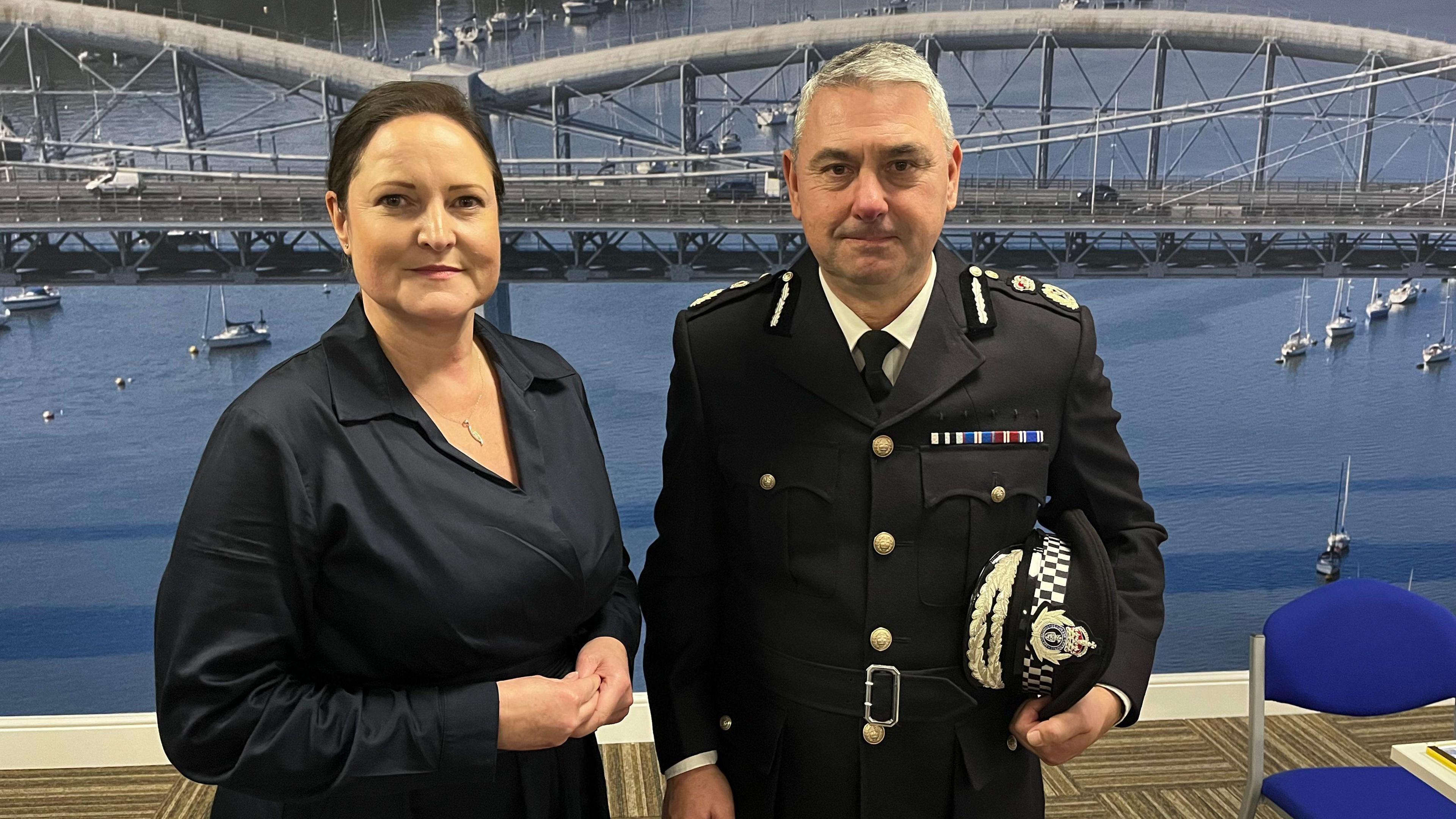 Alison Hernandez and new interim chief constable James Vaughan. The pair are stood side by side in front of a large image of the Royal Albert bridge. Mr Vaughan is dressed in uniform. Ms Hernandez is wearing a dark blouse.