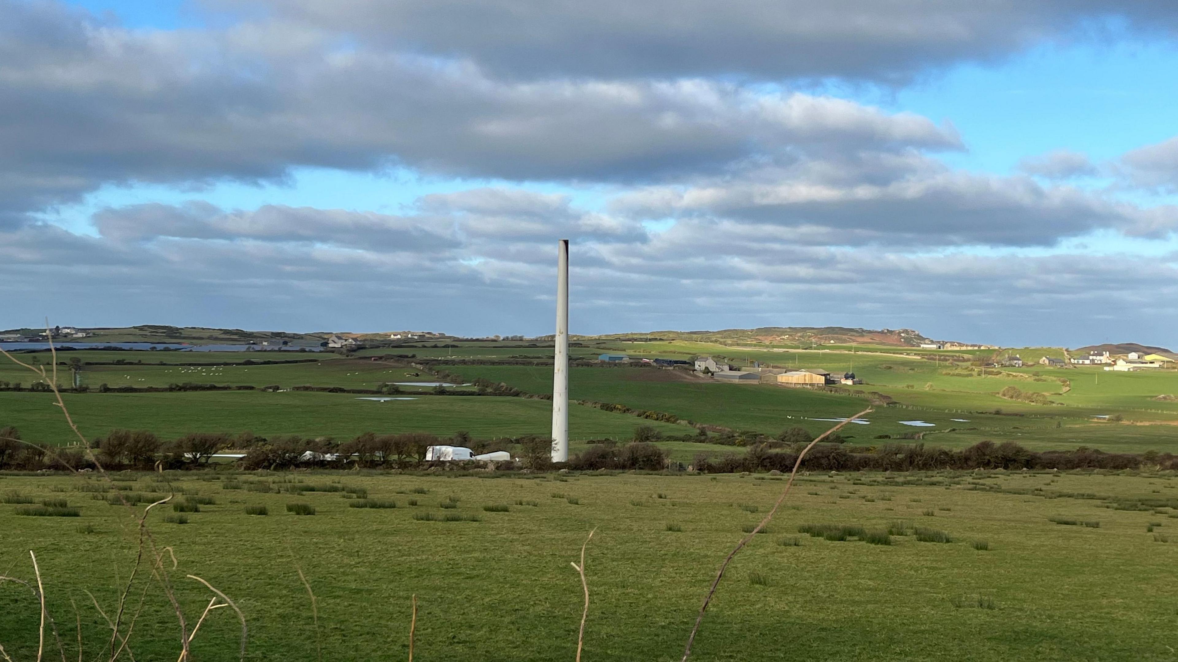 Wind turbine with missing blades. The pillar stands in the middle of a field and the top looks black.