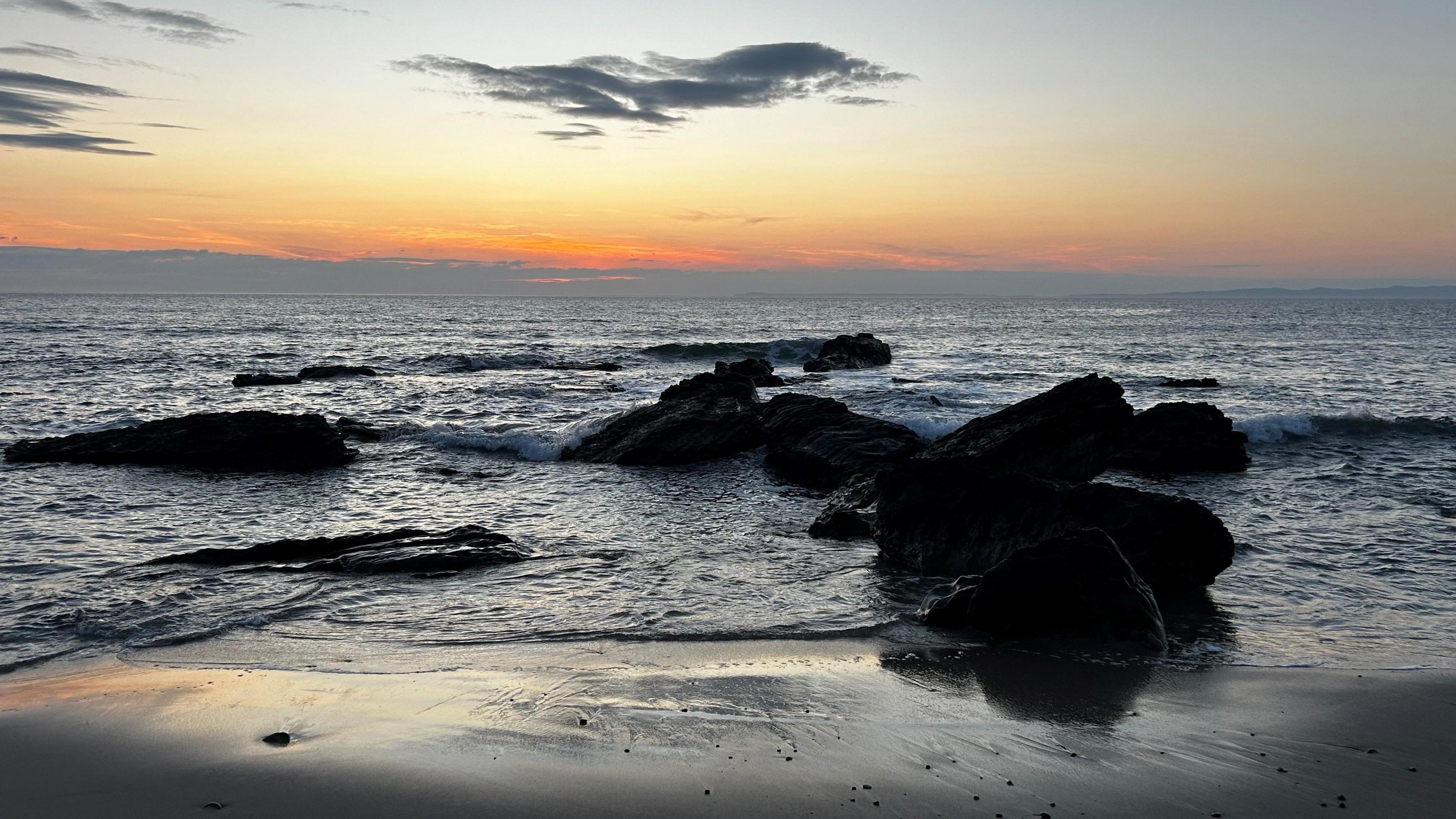 A view of rocks jutting out of water against and orange and yellow evening sky