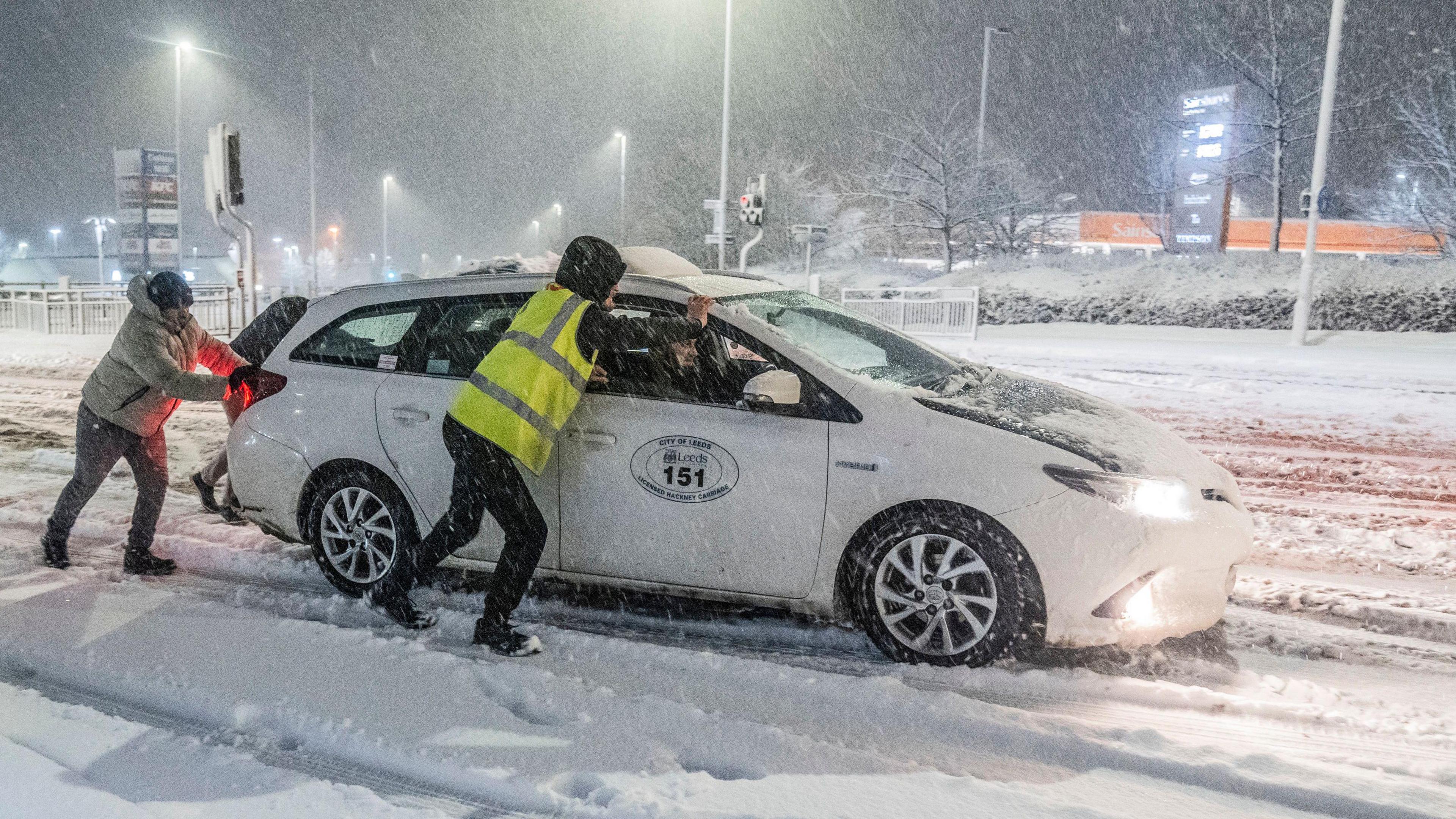 People help to push a taxi stuck in snow in Leeds.