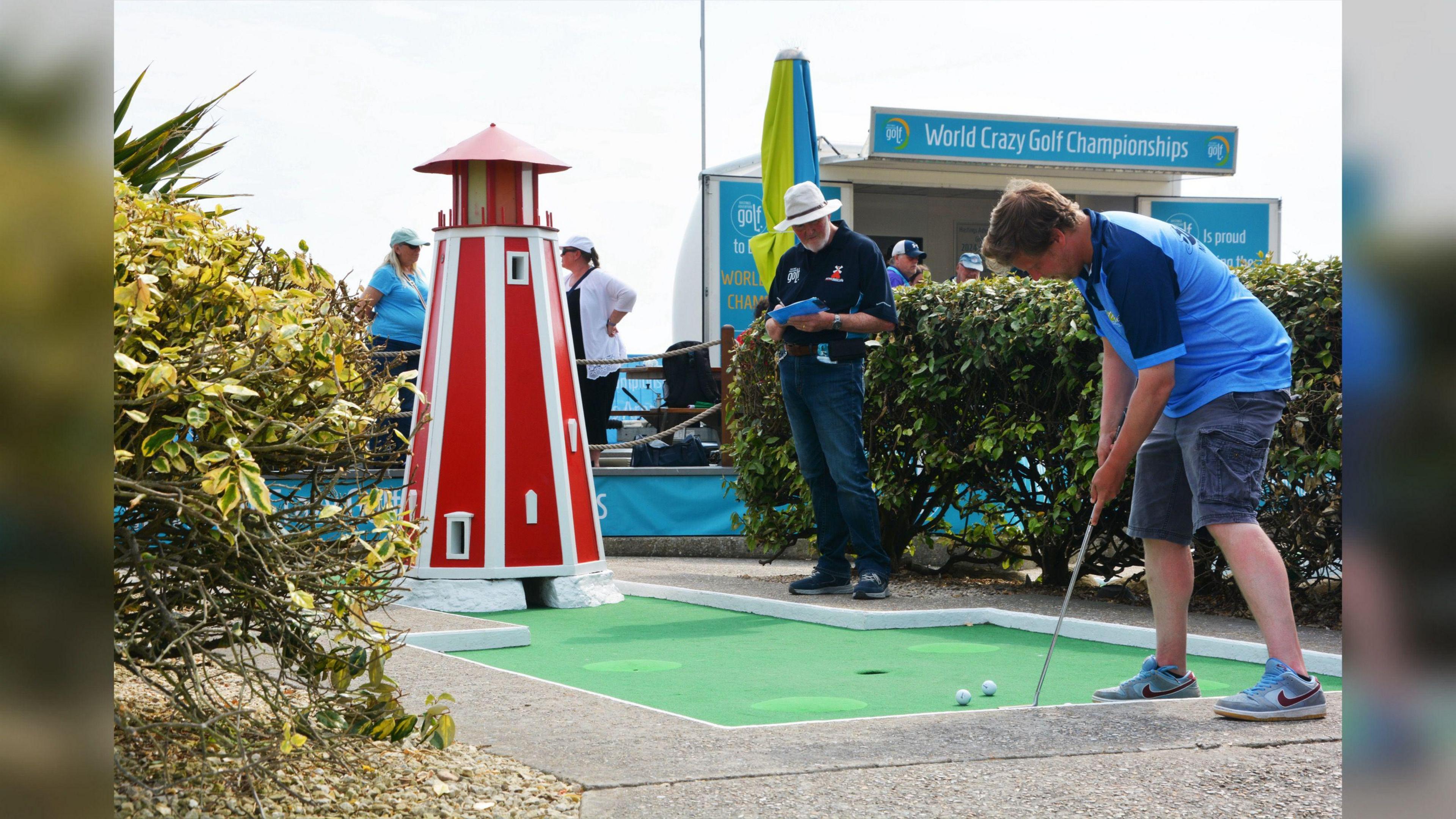 Someone lining up a shot by a miniature lighthouse