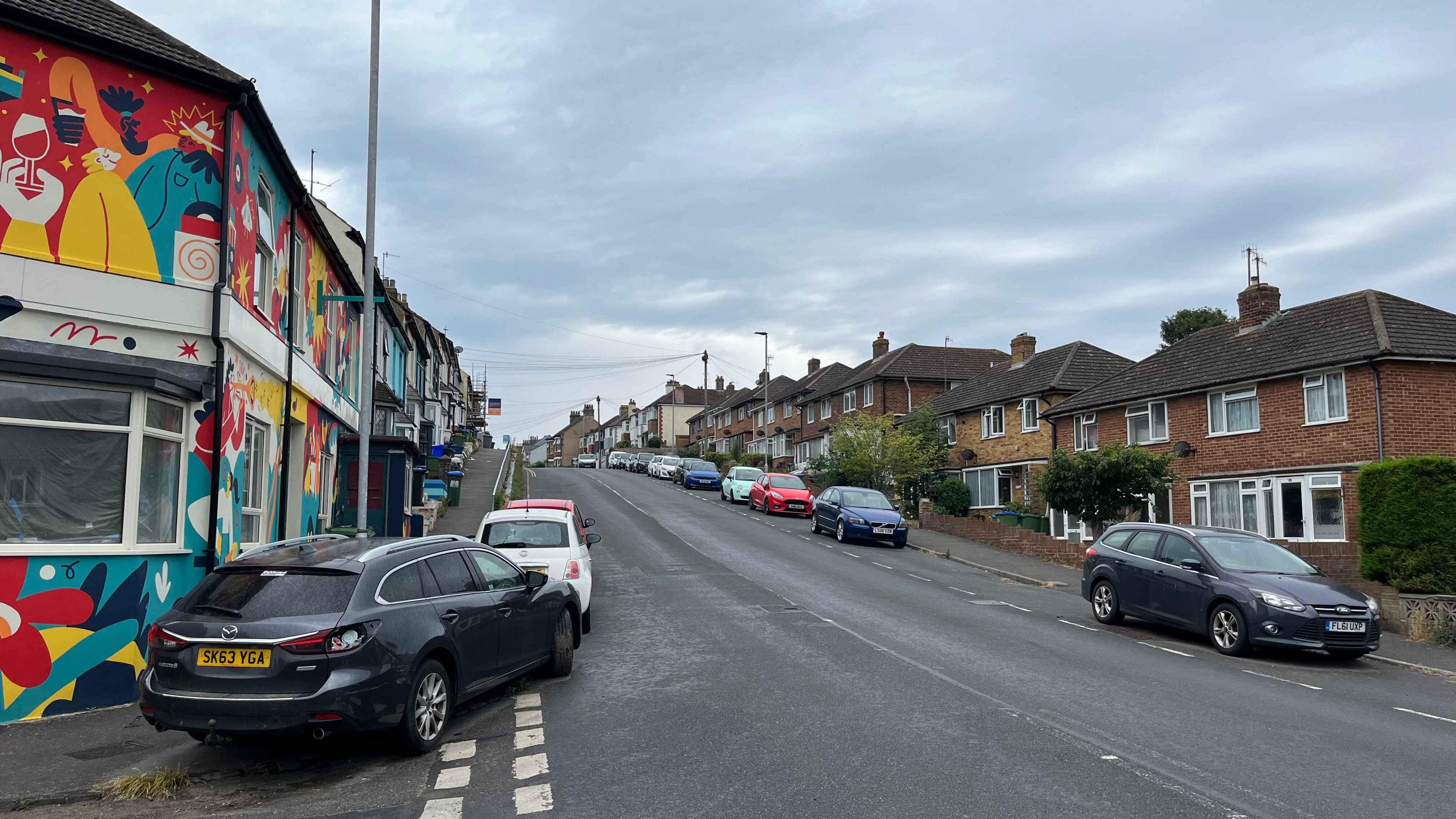 The bottom end of Lewes Road which has parked cars and houses on each side. It's at the bottom of a fairly steep hill with a blind crest at the top where you can't always see oncoming traffic