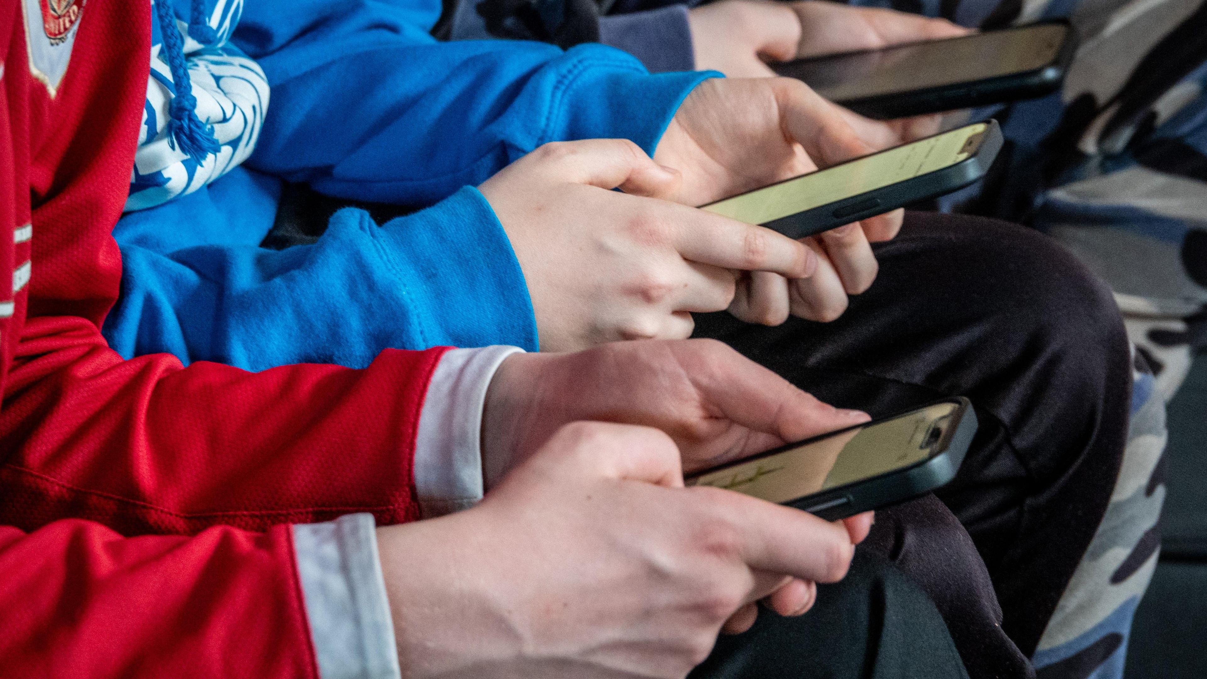 Tri o blant yn eu harddegau yn edrych ar sgriniau eu ffonau clyfar