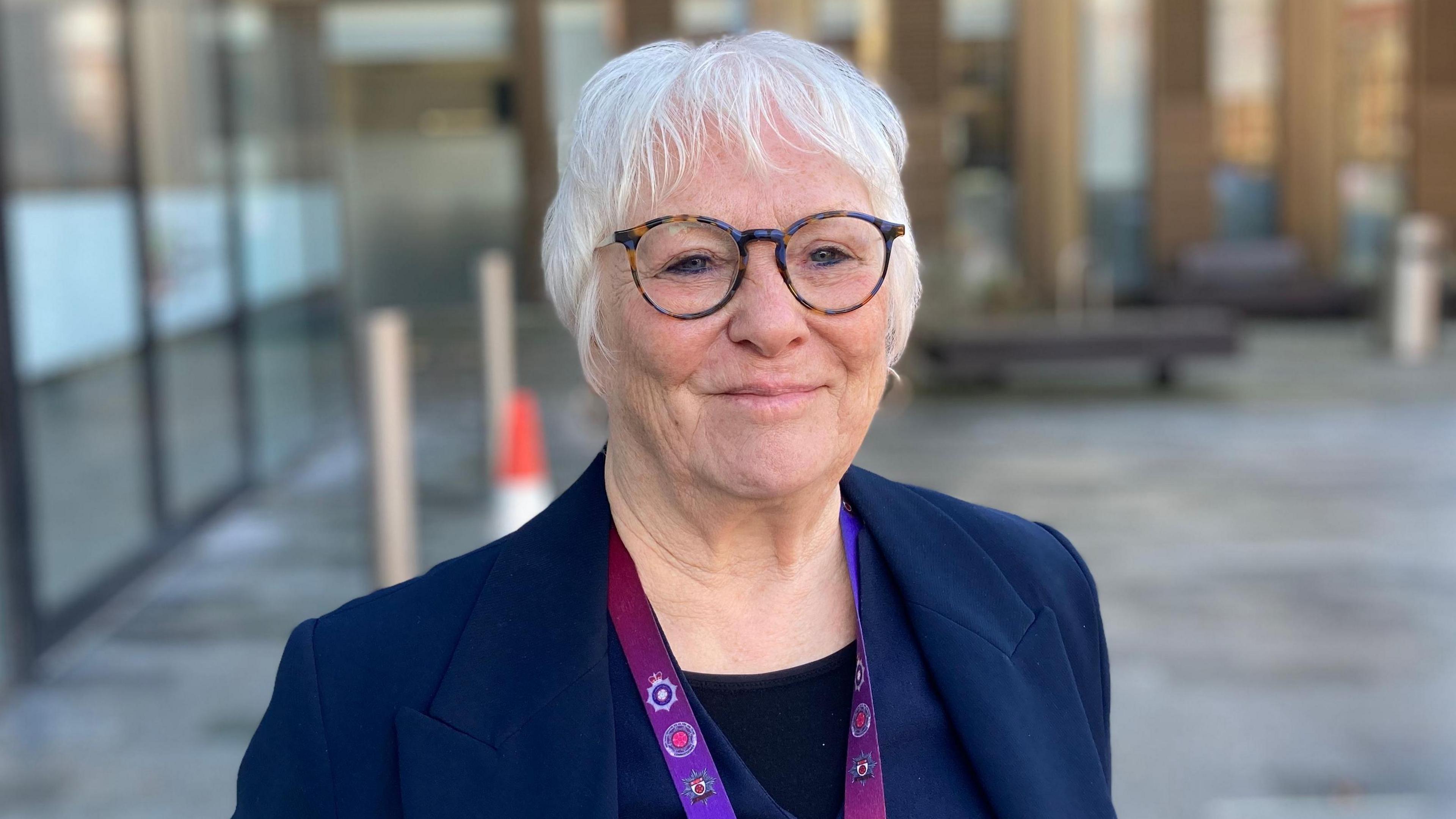 woman with navy jacket and glasses standing outside office building