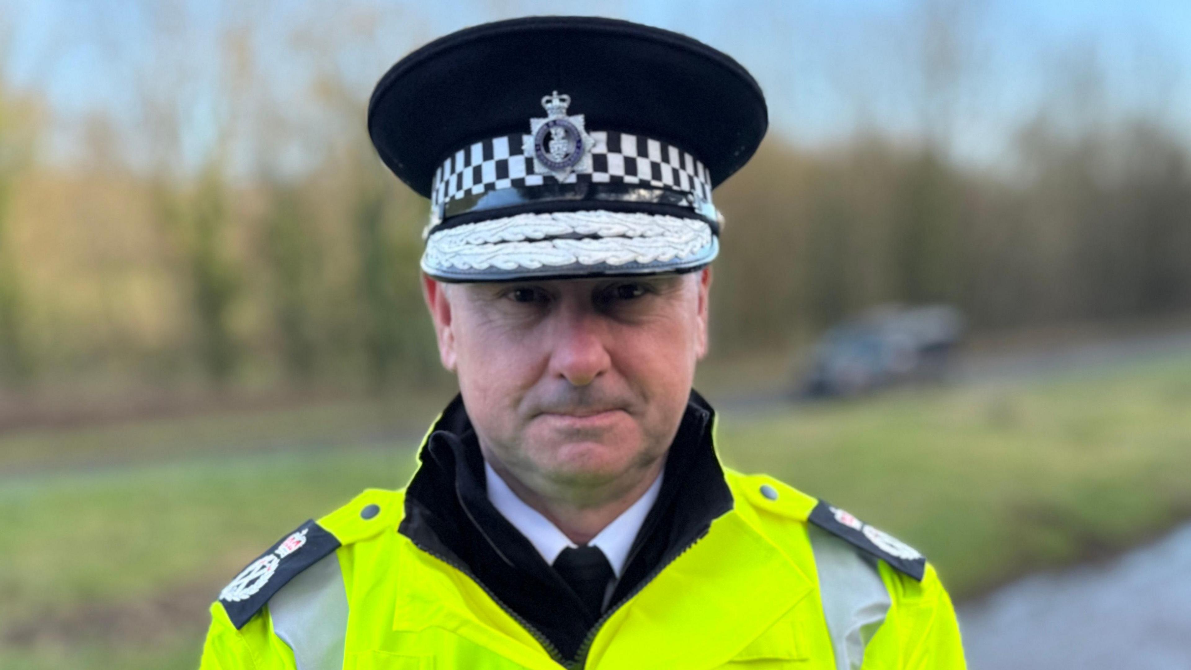 A police officer in full uniform wearing a high vis jacket standing in a field.