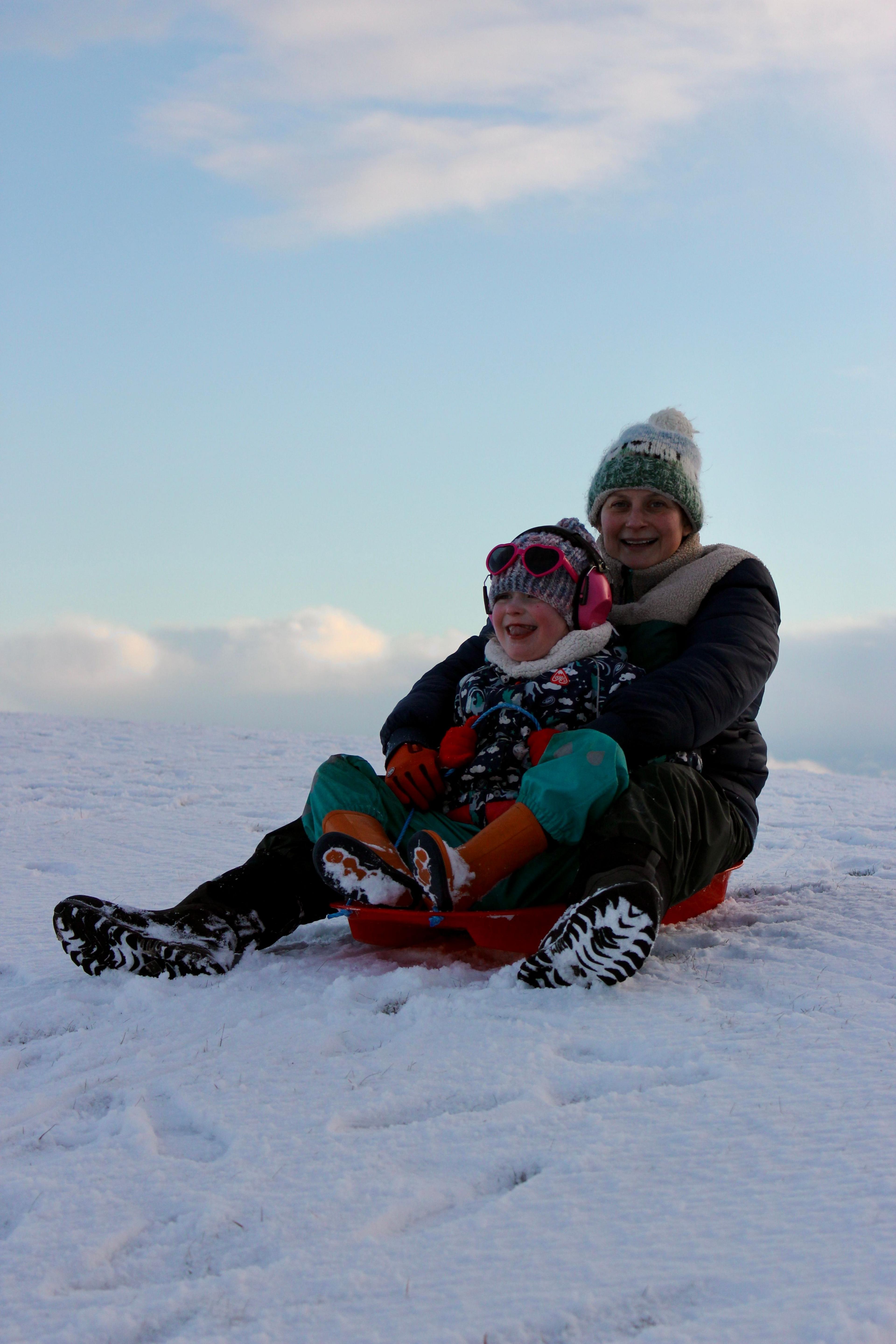 Boireannach agus pàiste air slaodan san t-sneachd ann an Uibhist 