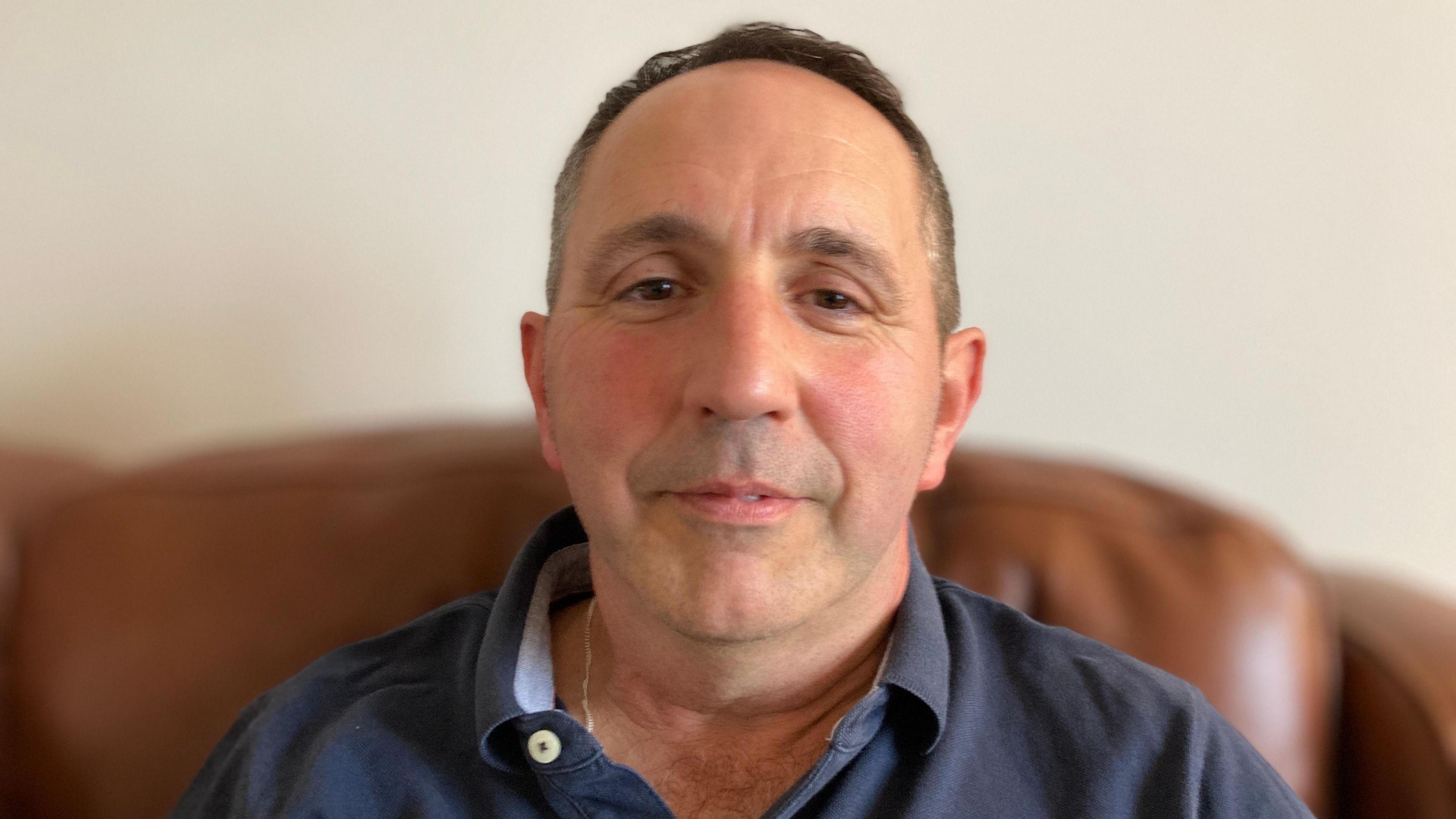 Mark is looking directly into camera and sitting at home in Oakham.