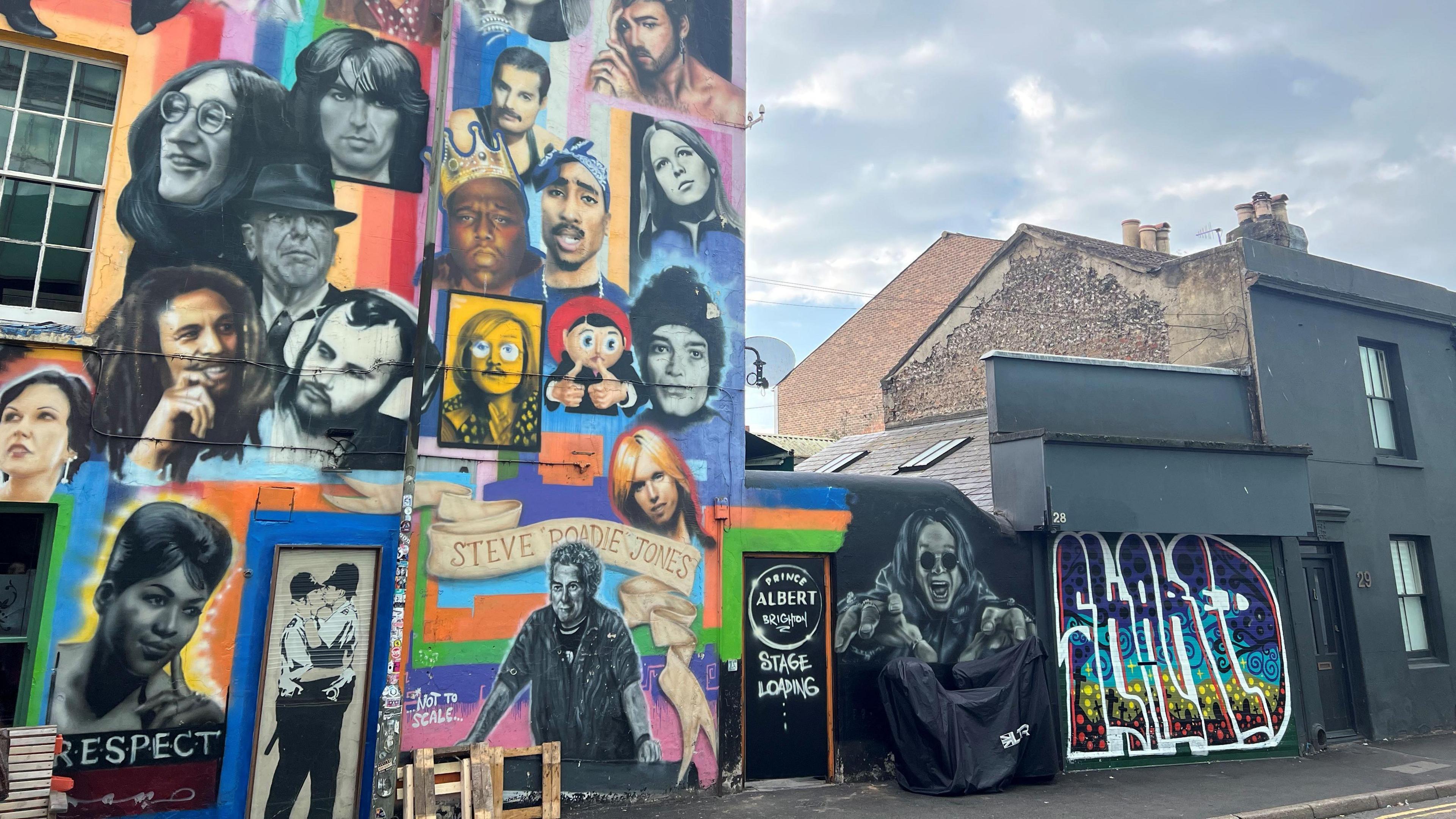 A multi-coloured wall of murals with lots of people painted on it.