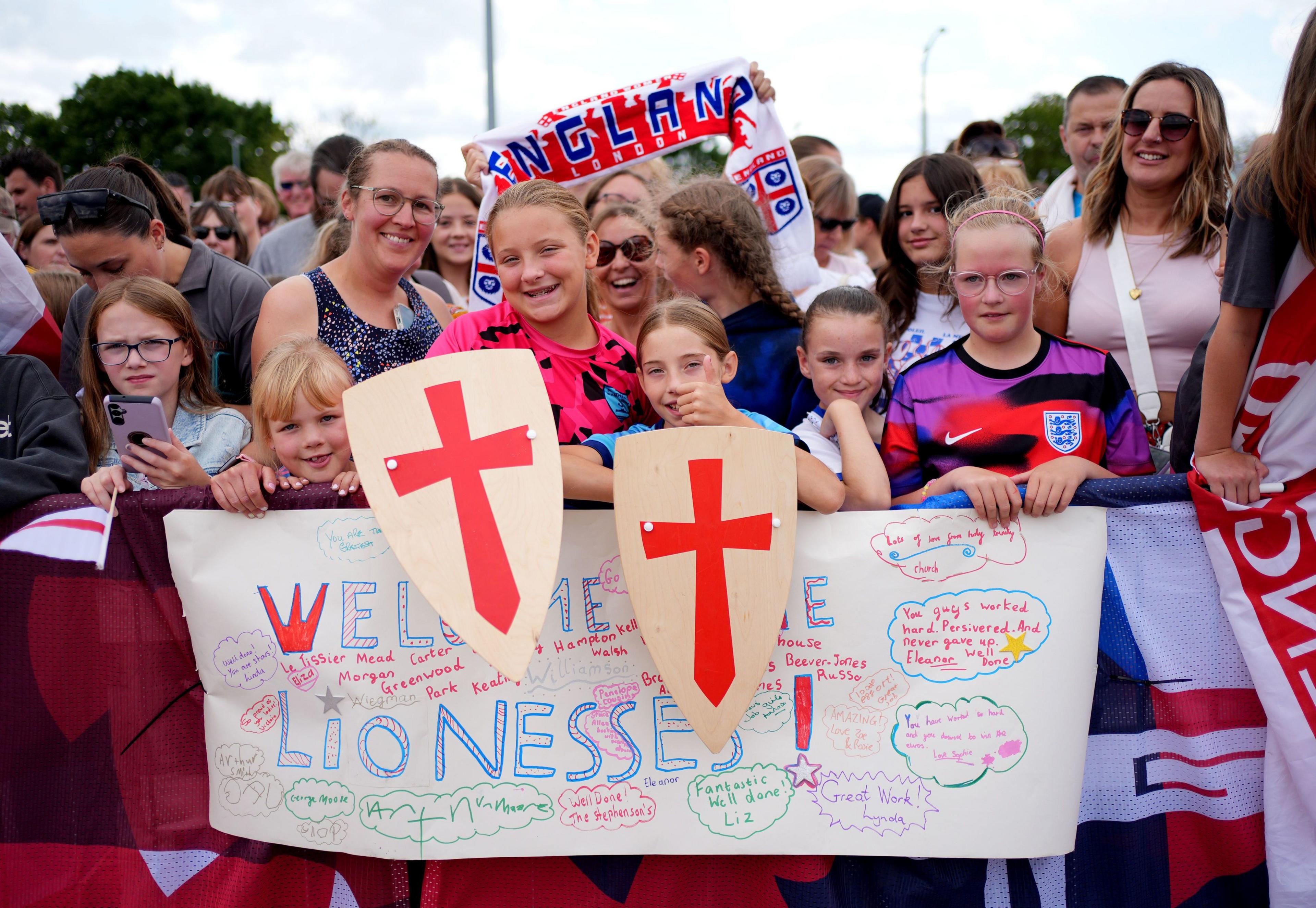 fans with a homemade banner that reads welcome lionesses smiling while waiting for the lionesses to walk past