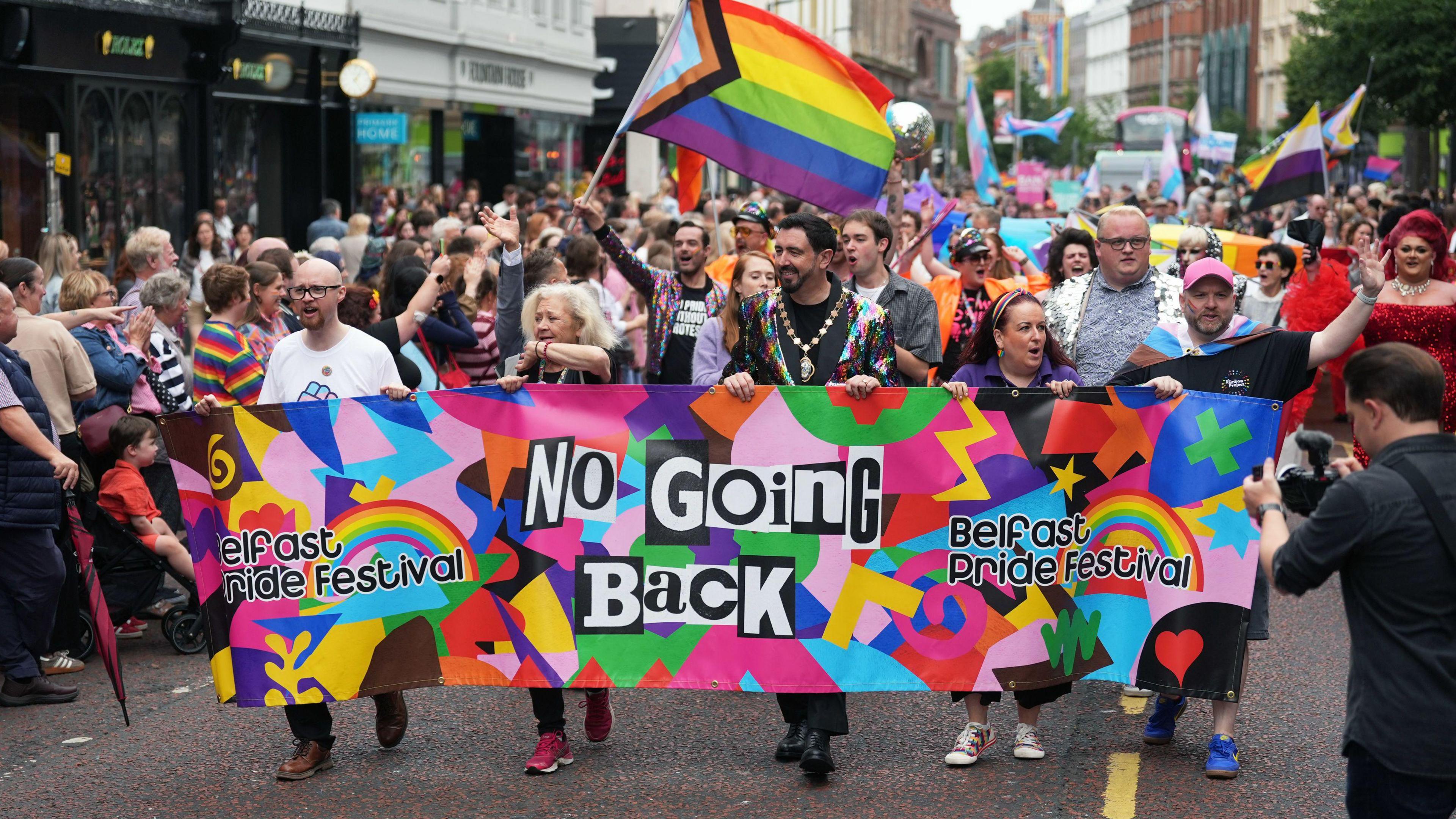 People take part in the 2025 Belfast Pride Parade, in the city centre. They hold a banner saying ''No Going Back'' and wave LGBT+ flags.
