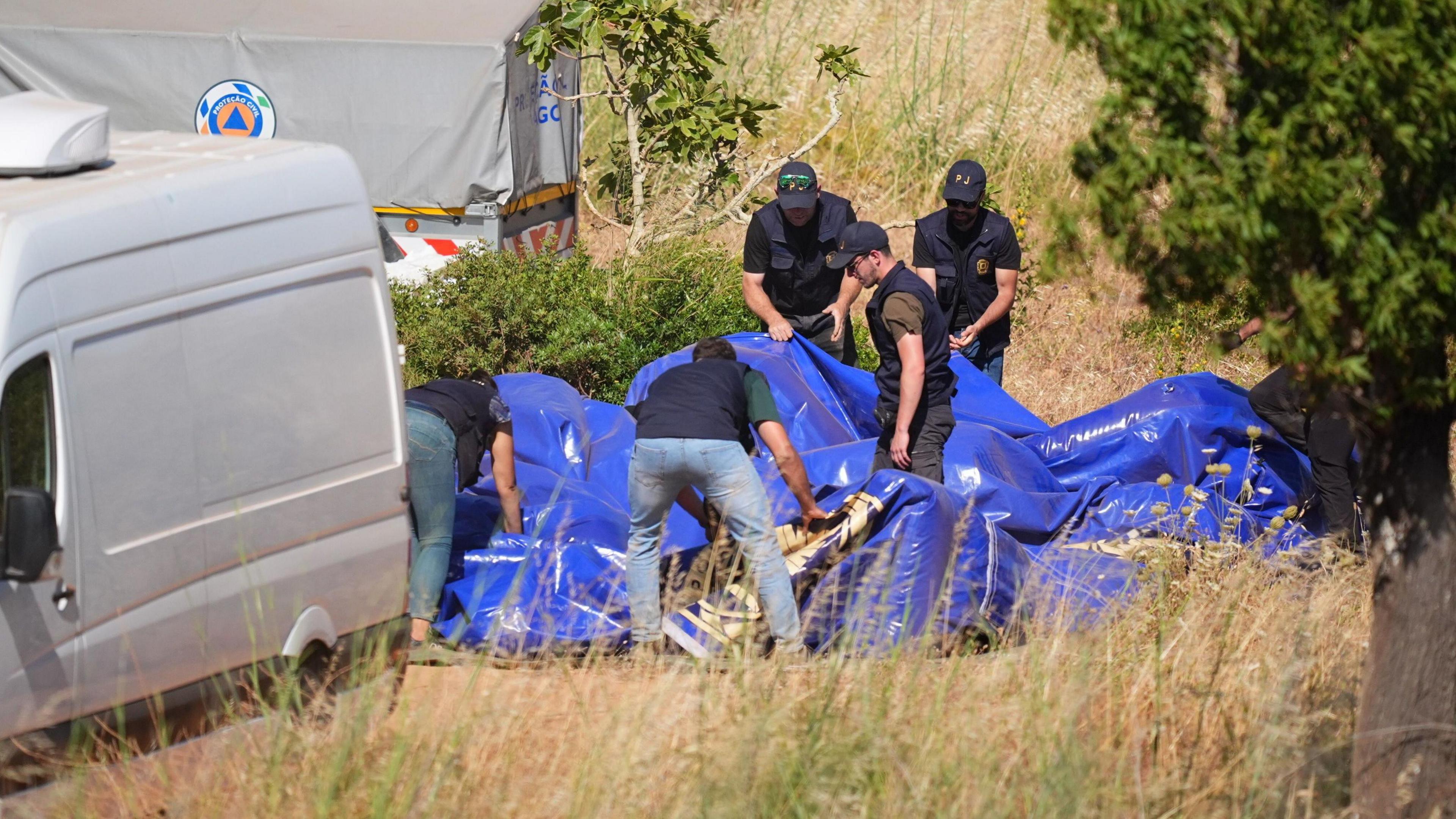 Five members of the search operation pull down a blue tent.