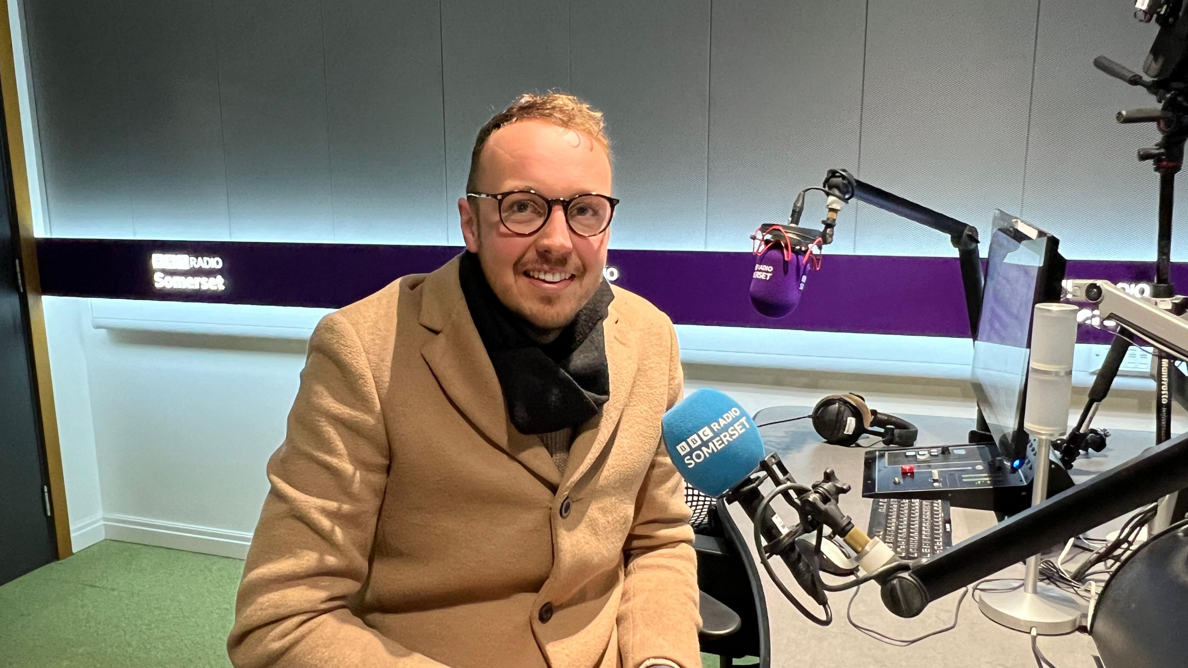 Adam Dance MP sat in a radio studio in front of a microphone looking at the camera