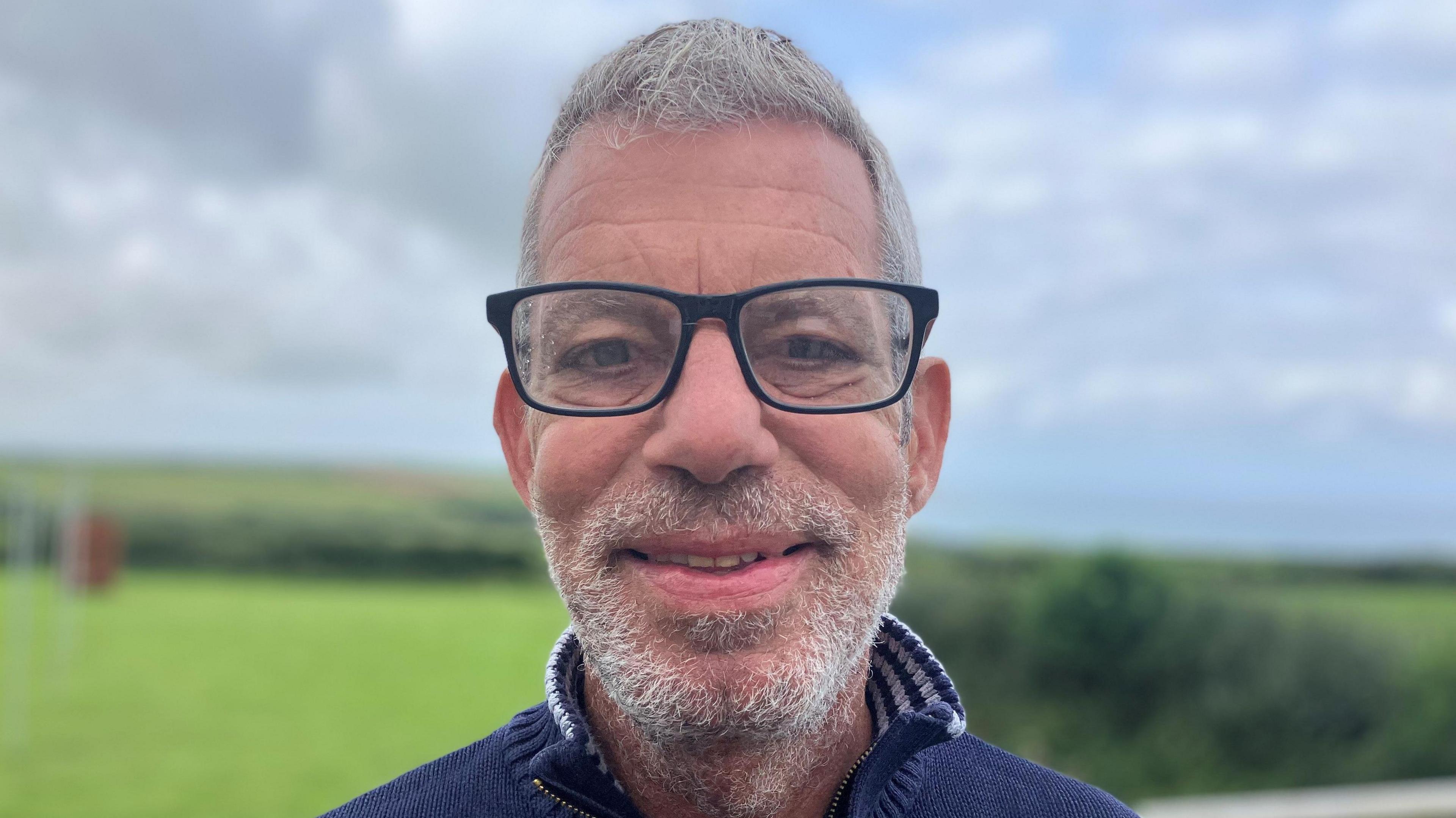 Mark Benattar, with glasses, standing in a location where you can see Port Isaac Bay behind 