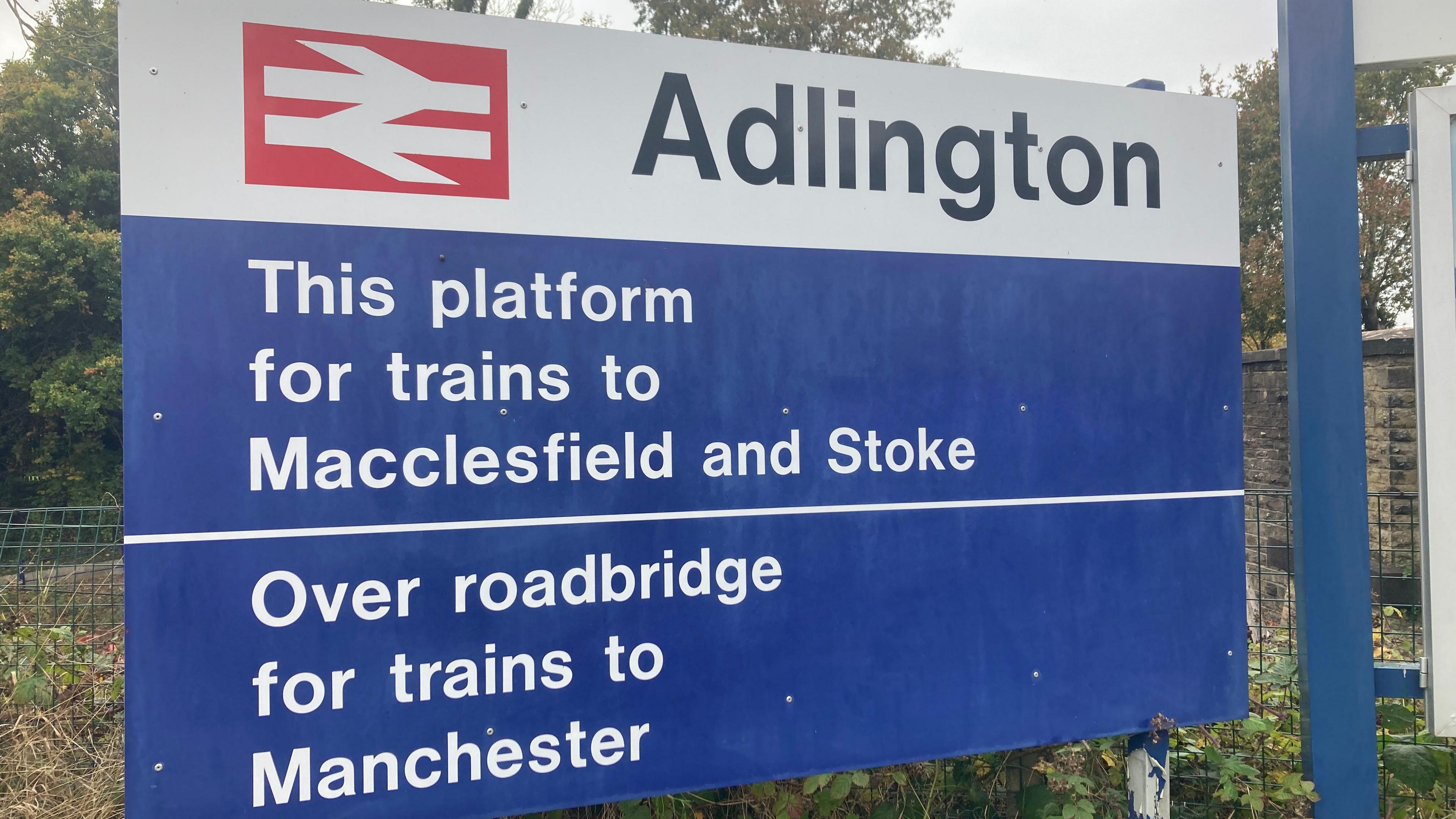 A view of the sign at Adlington Railway Station. It says this platform for trains to Macclesfield and Stoke and over roadbridge for trains to Manchester.