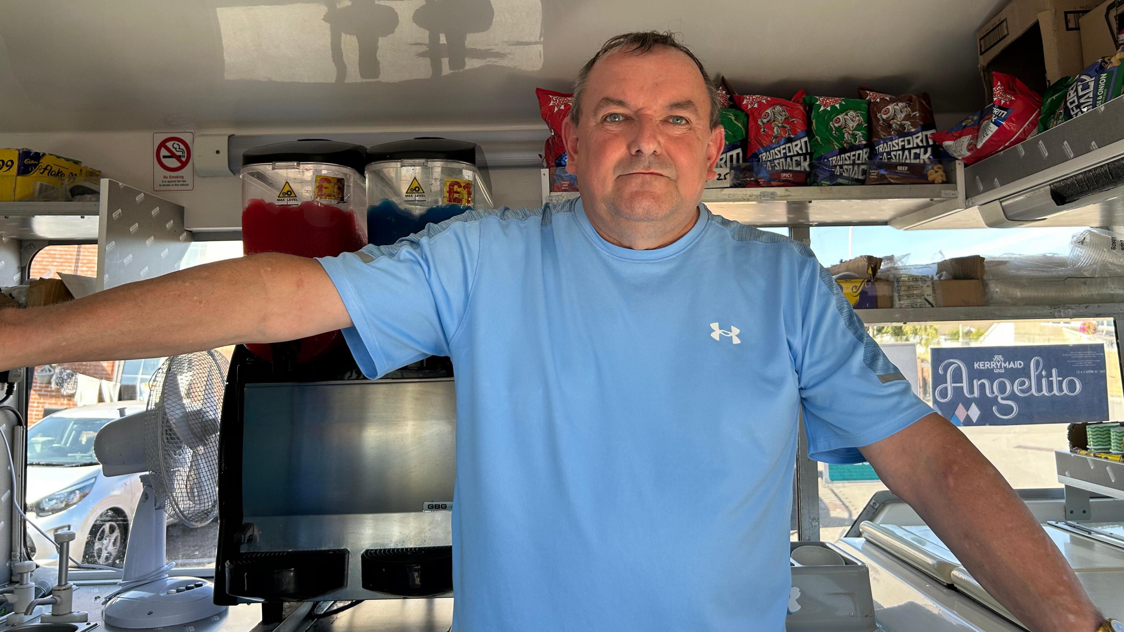 Mark Edwards in his ice cream van. He is wearing a blue t shirt and looking at the camera