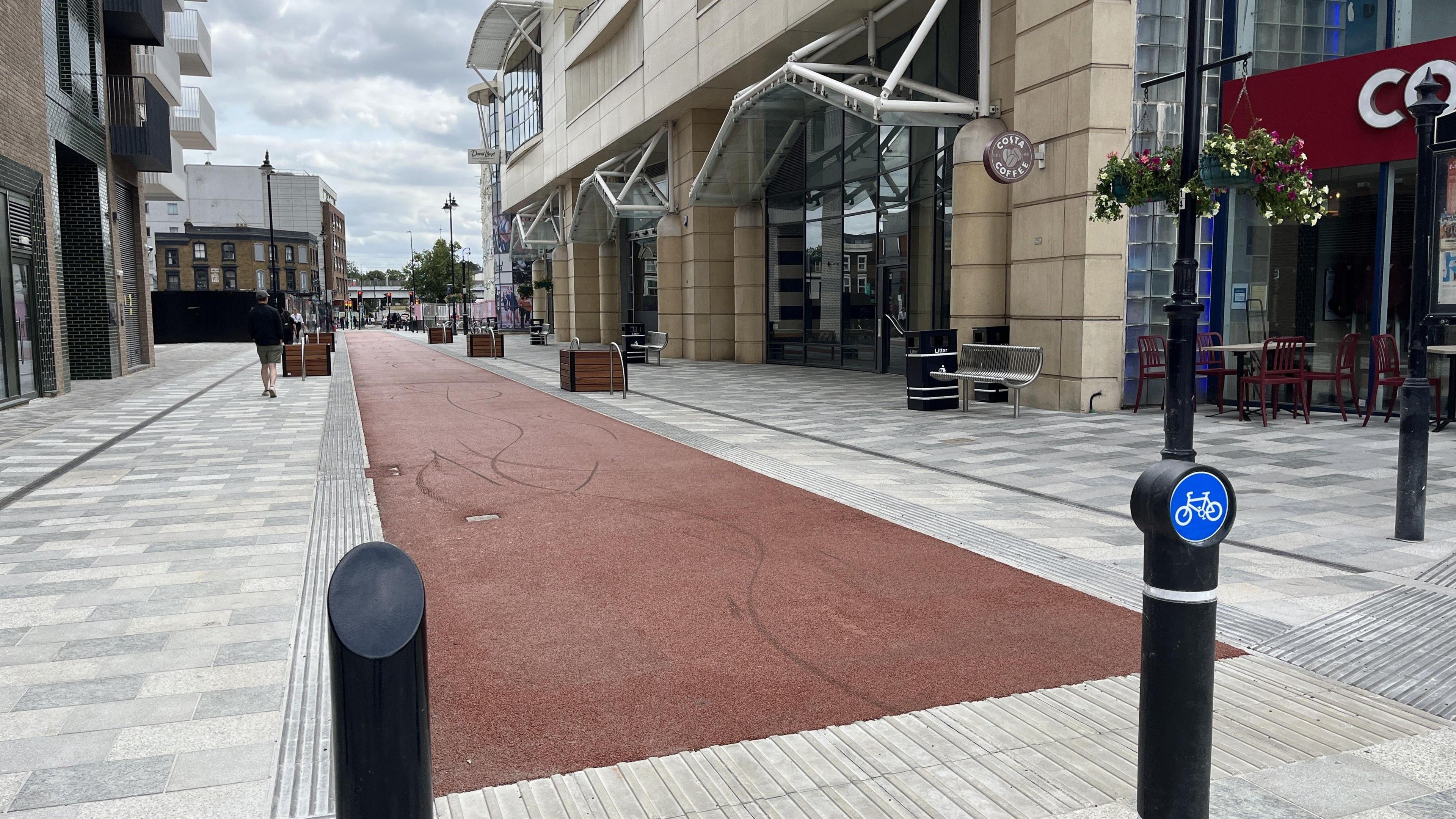 A red cycle path, with bollards next to it, bordered by paths for walking 