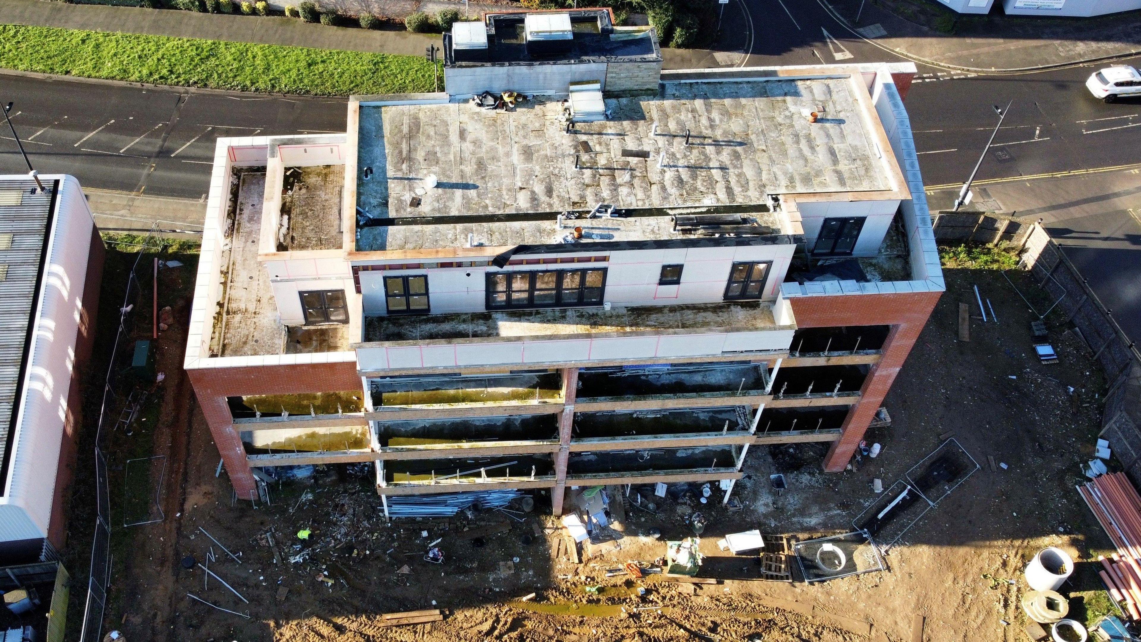 Tollesbury House, a five-storey block of flats which remains unfinished, from above. Some moss is growing on some of the balconies and there is building material which surrounds the incomplete building.