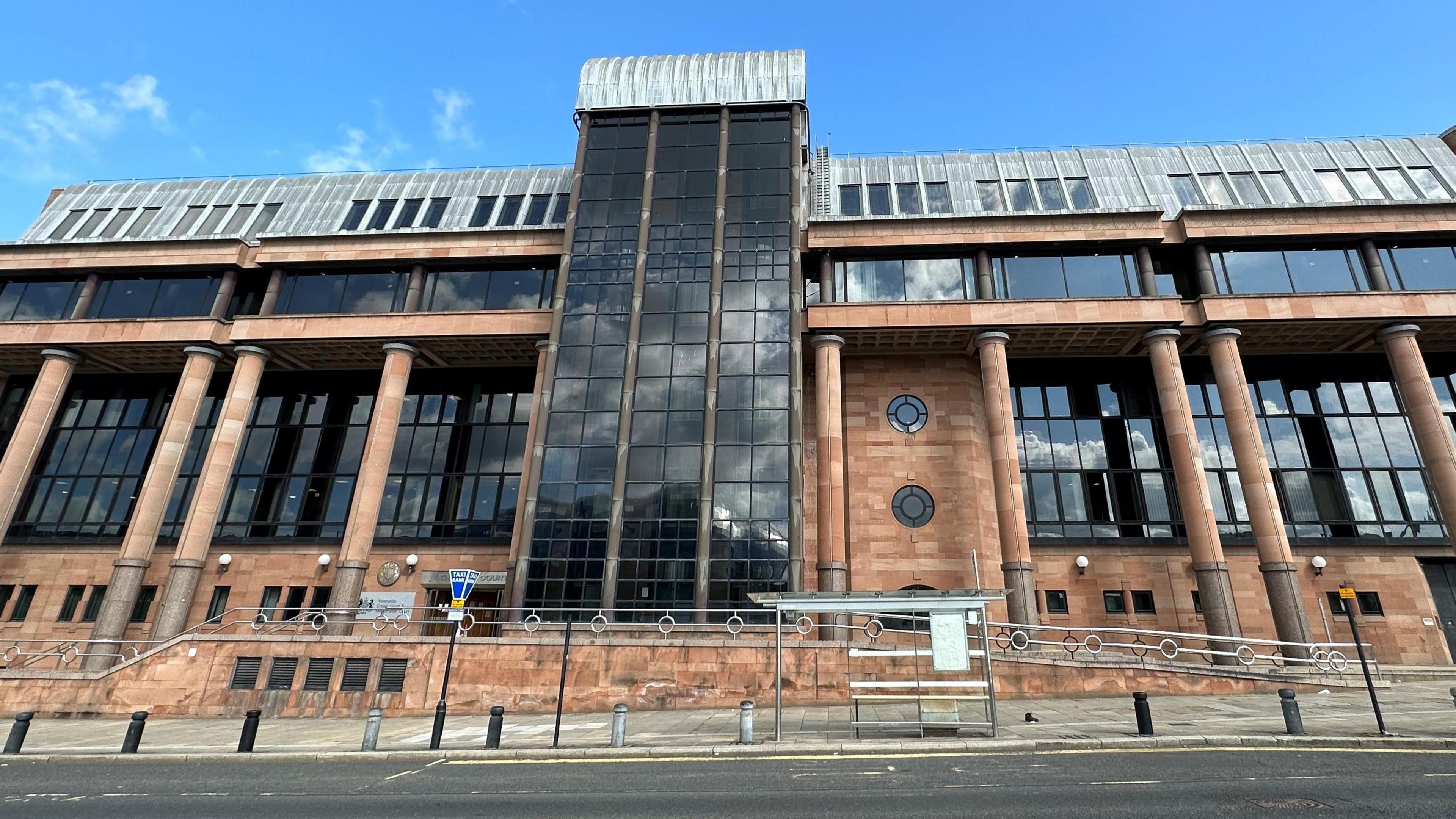 Imposing court building made from red stone walls and columns with large dark windows.