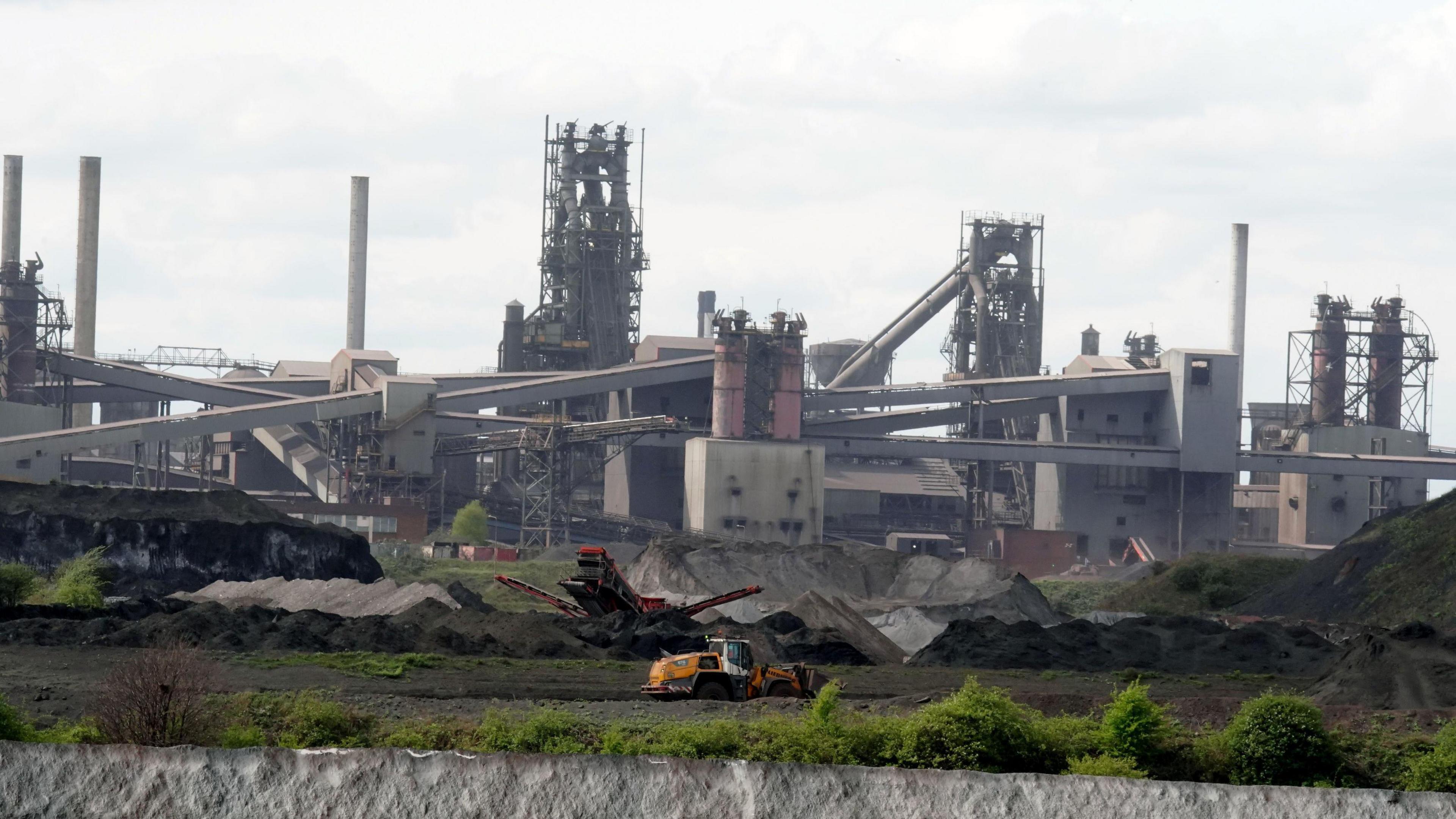The blast furnaces at the steelworks in Scunthorpe. A yellow digger is in the foreground scooping up material to be taken into the site.