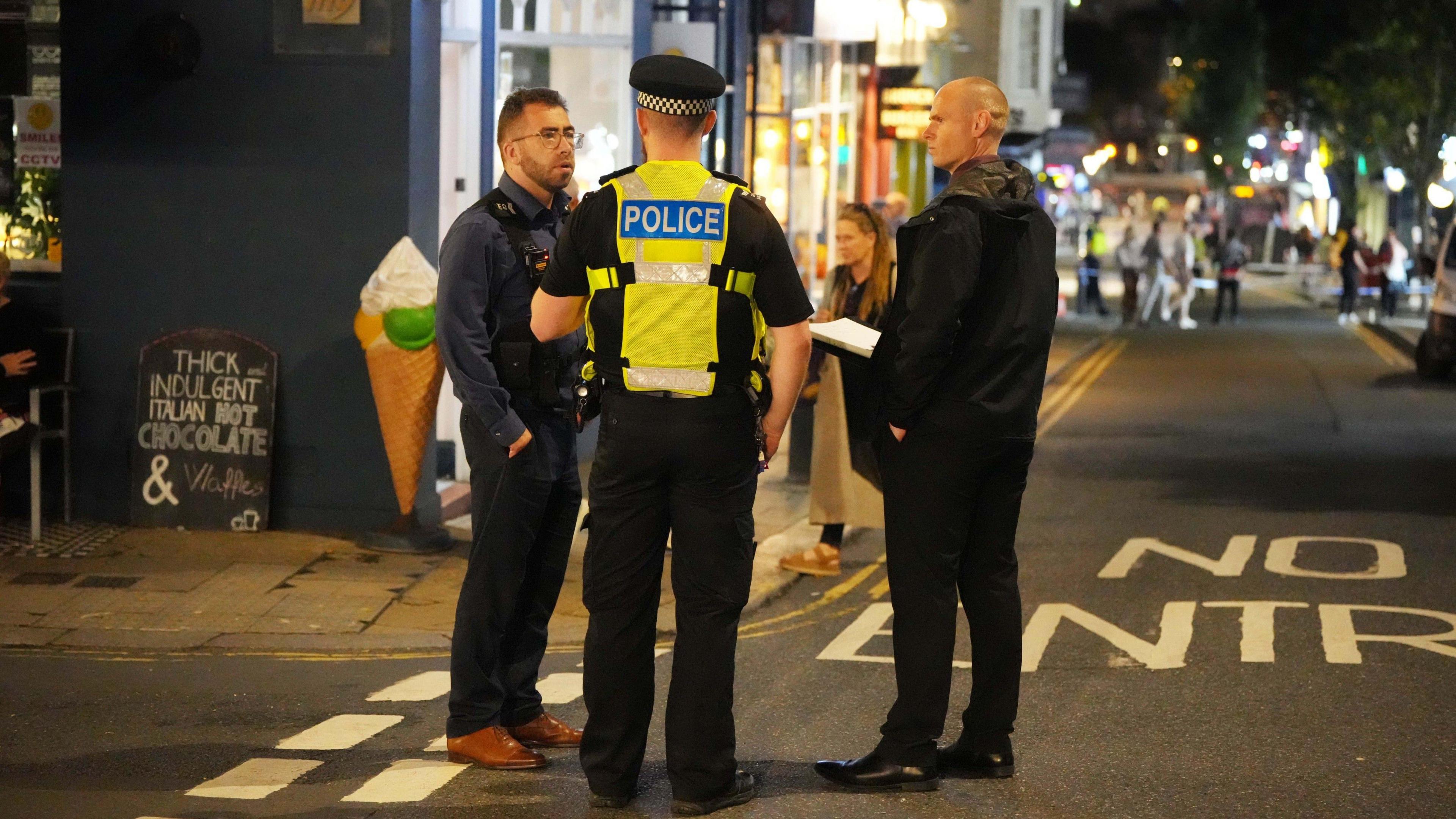 Three police officers stand on the street in a taped off area of St James Street, Brighton