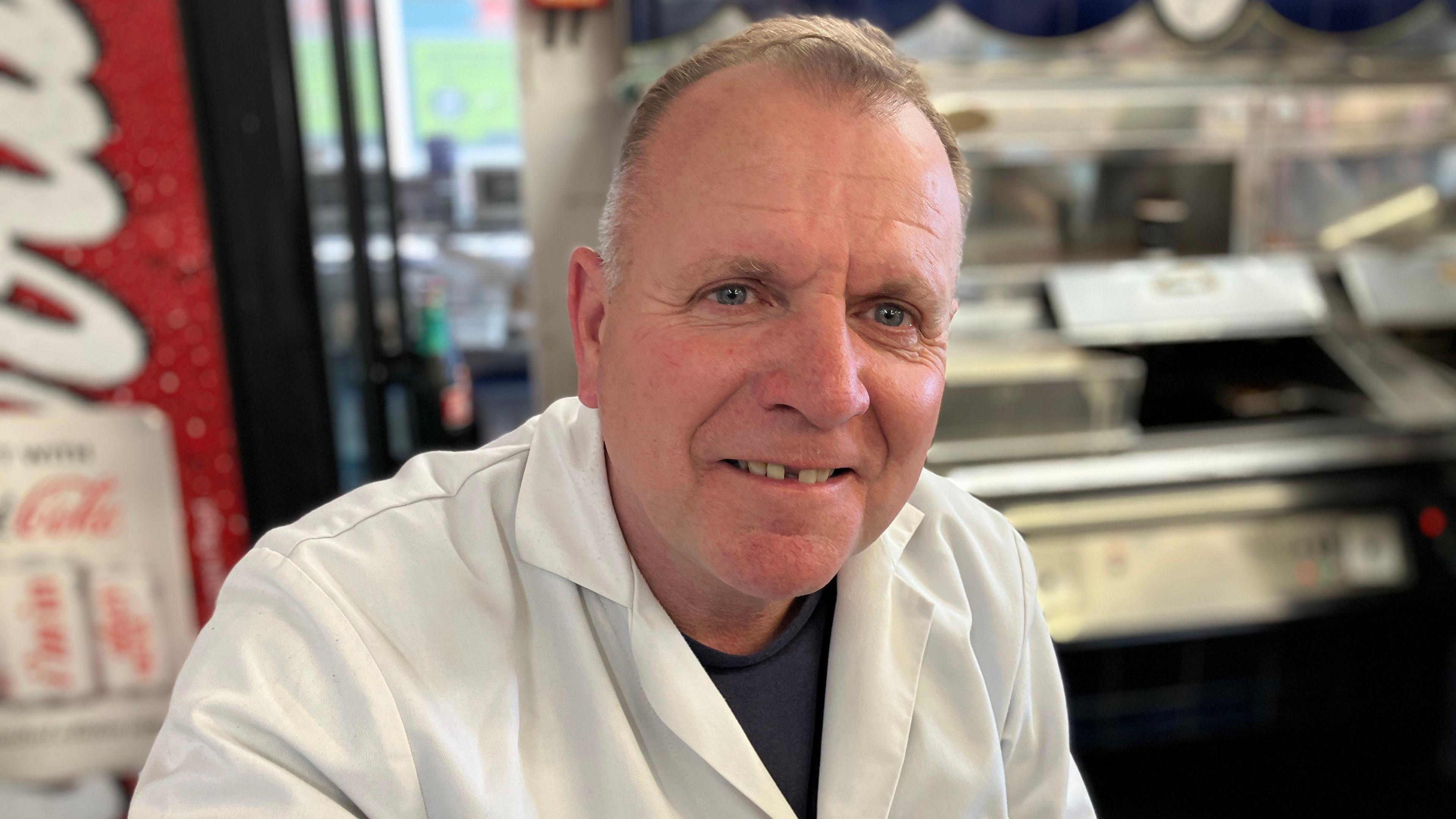 Peter McGowan wearing a white work jacket in front of fiosh and chip counter