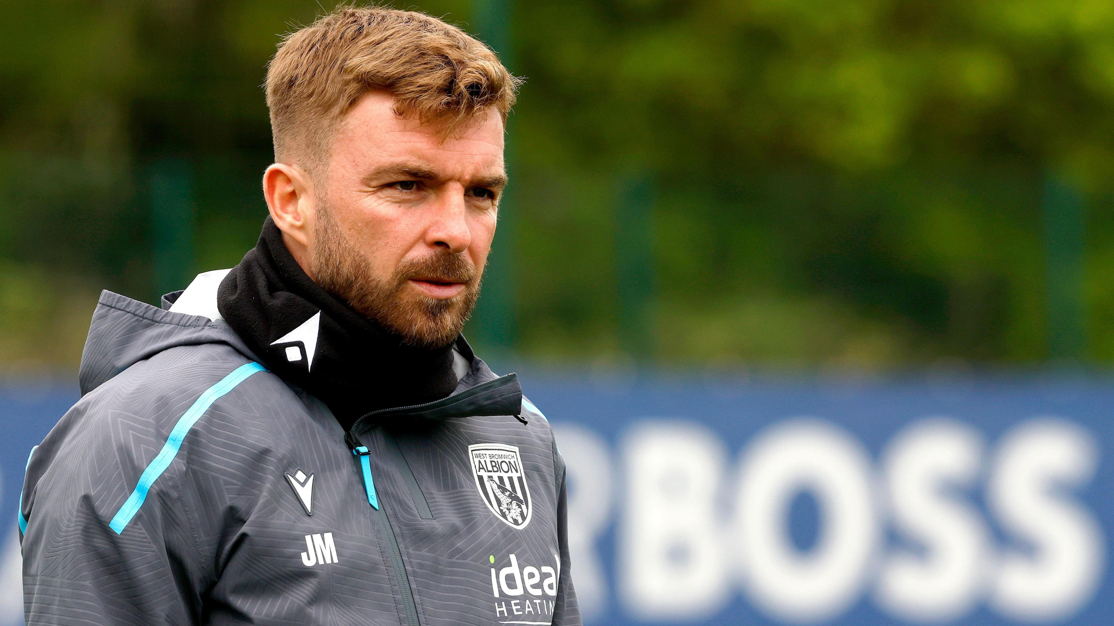 James Morrison wearing a grey West Bromwich Albion tracksuit top and black snood while in a training session with the word "BOSS" seen on a blurred advertising board in the distance behind him.