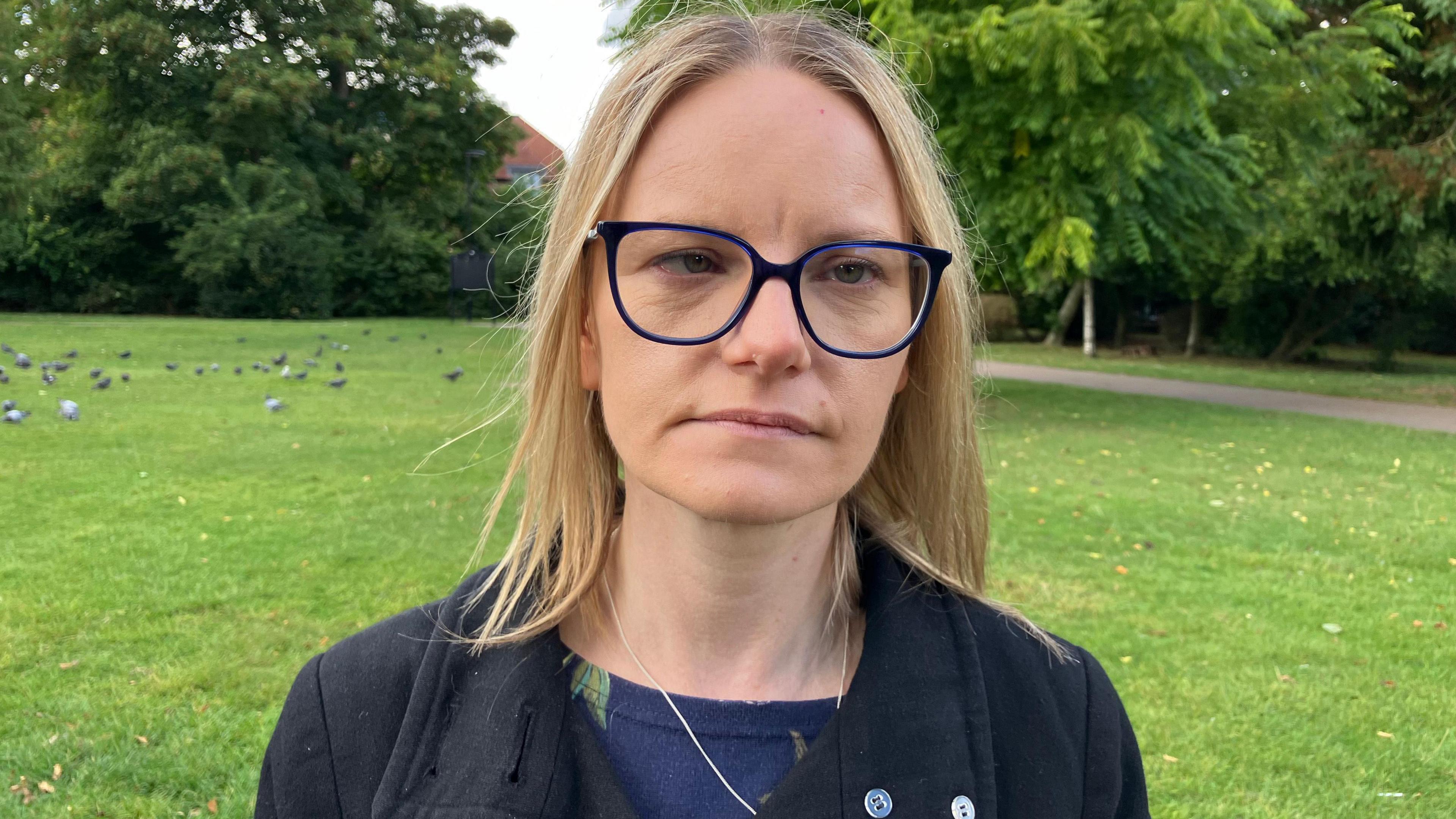 Woman with glasses and a black coat, outside in a park