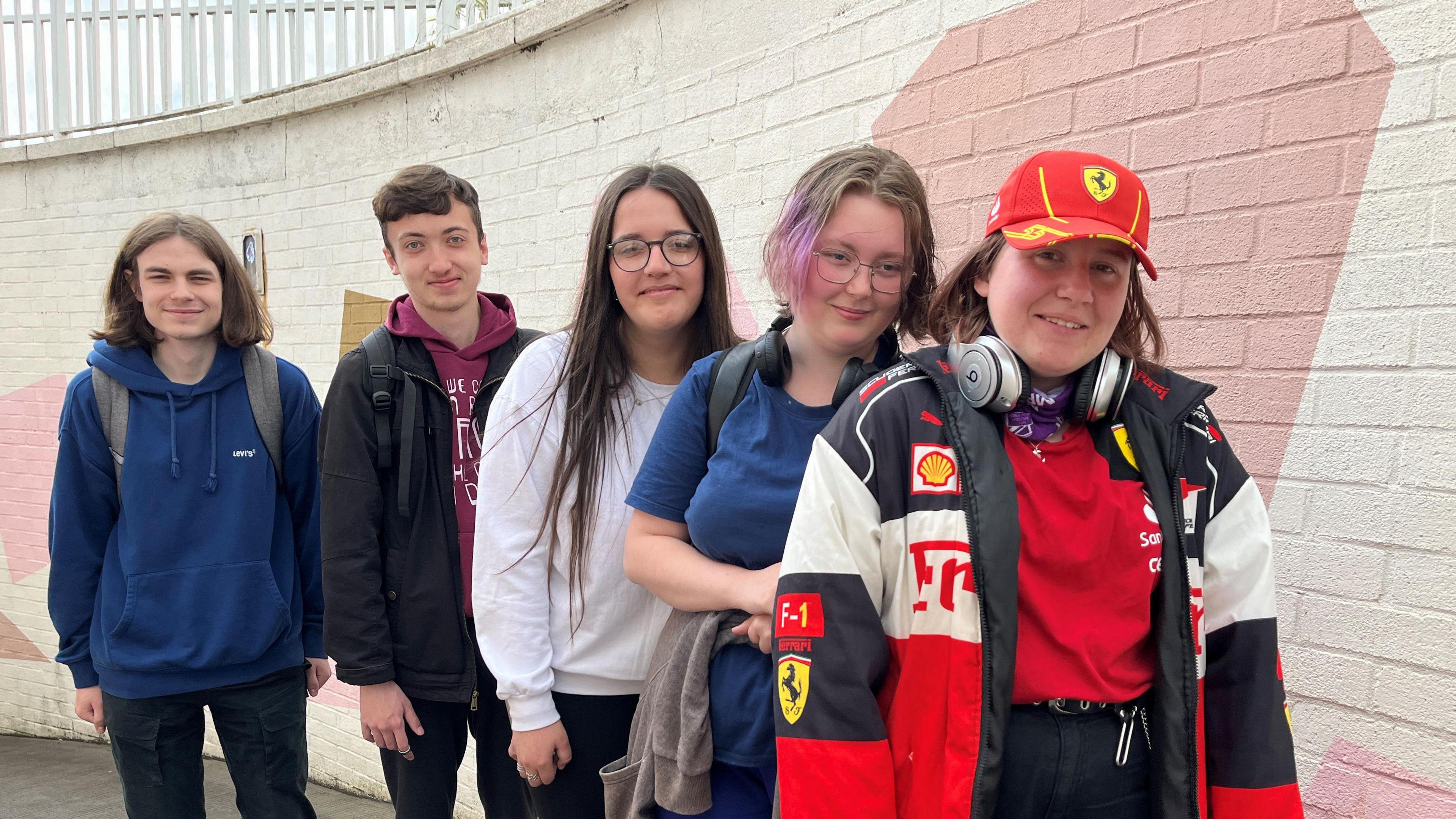 Aaron, Leo, Leonor, Ink and Kayley, stand in a line against an underpass wall