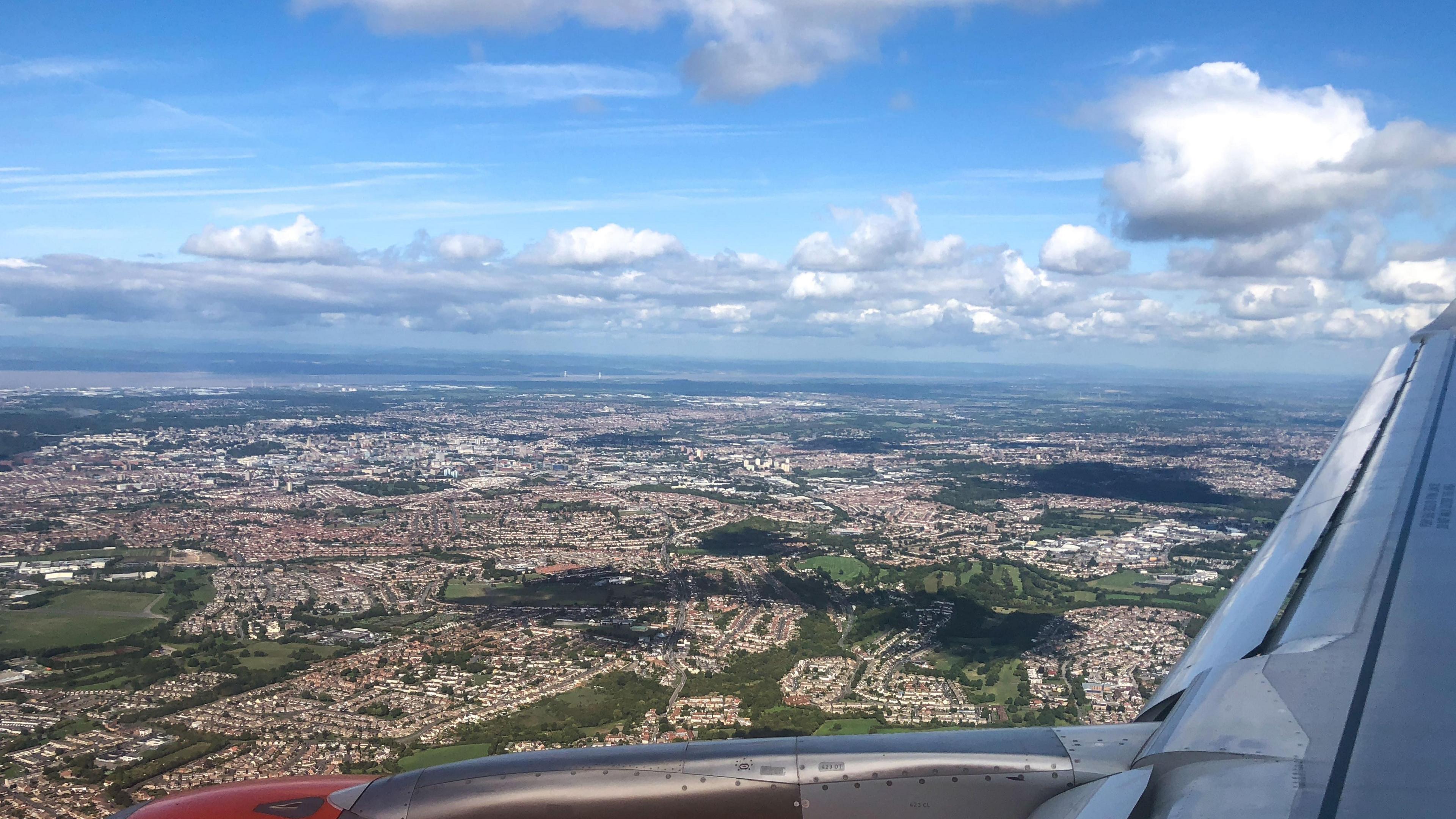 A birds-eye view of the land below, from the wing of a plane. It is a clear day with a few white clouds dotted around.