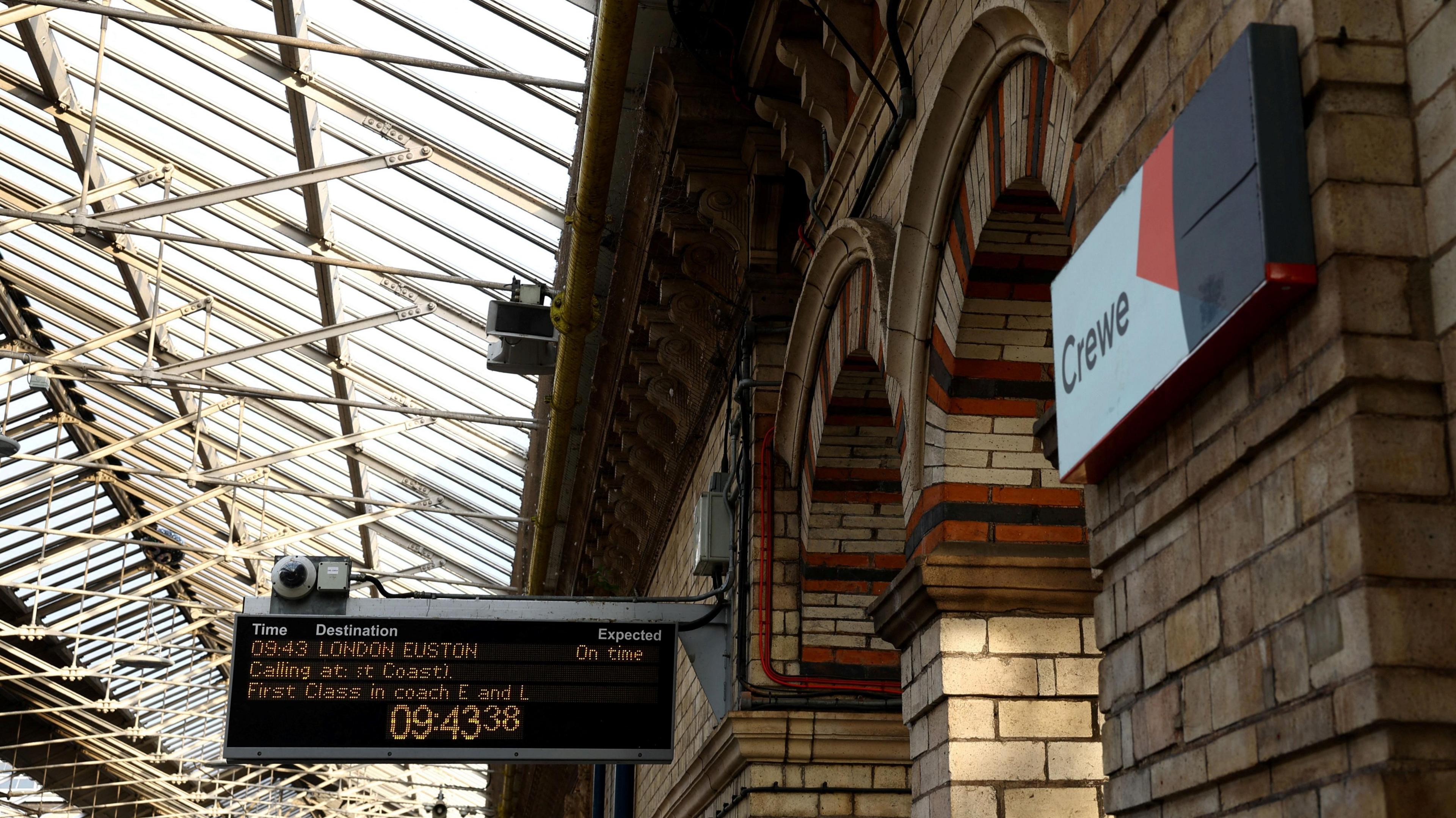 A view of Crewe Station. There's a sign saying Crewe on the wall and a information board for a train to London Euston.